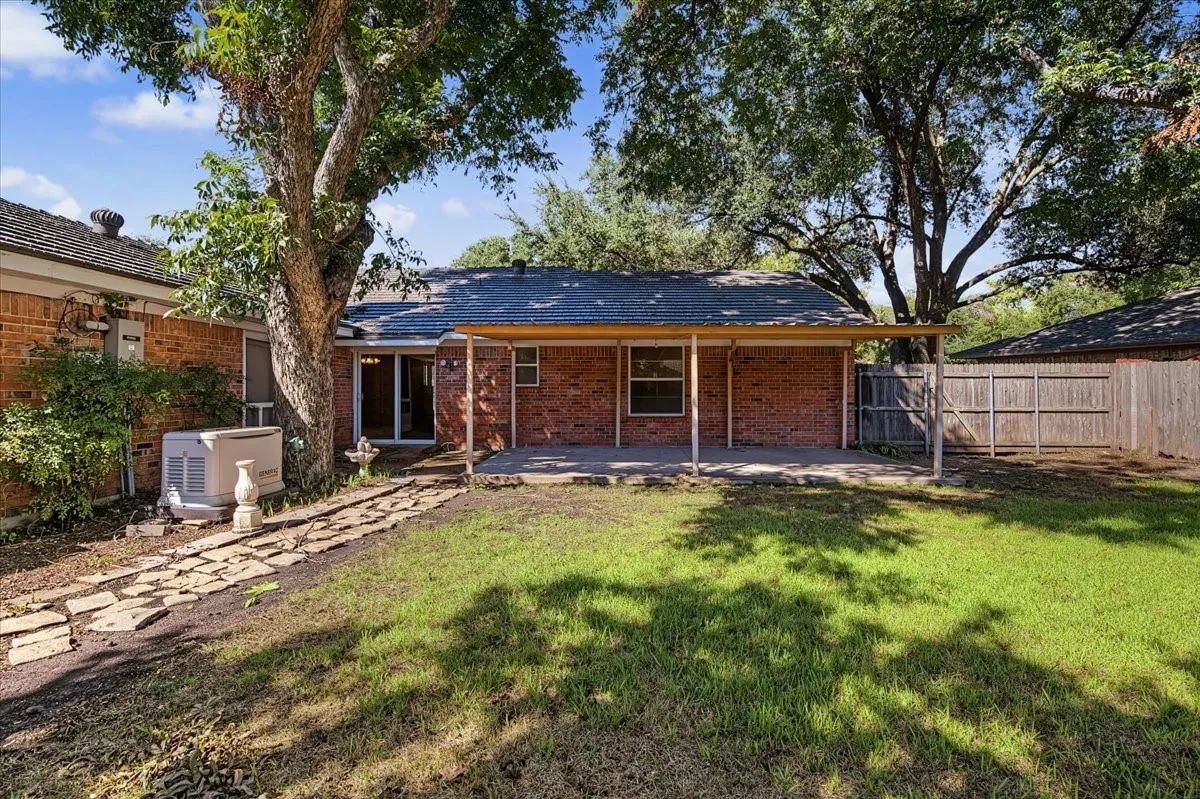 Brick exterior with a covered patio, wood fencing, and a stone-paver pathway