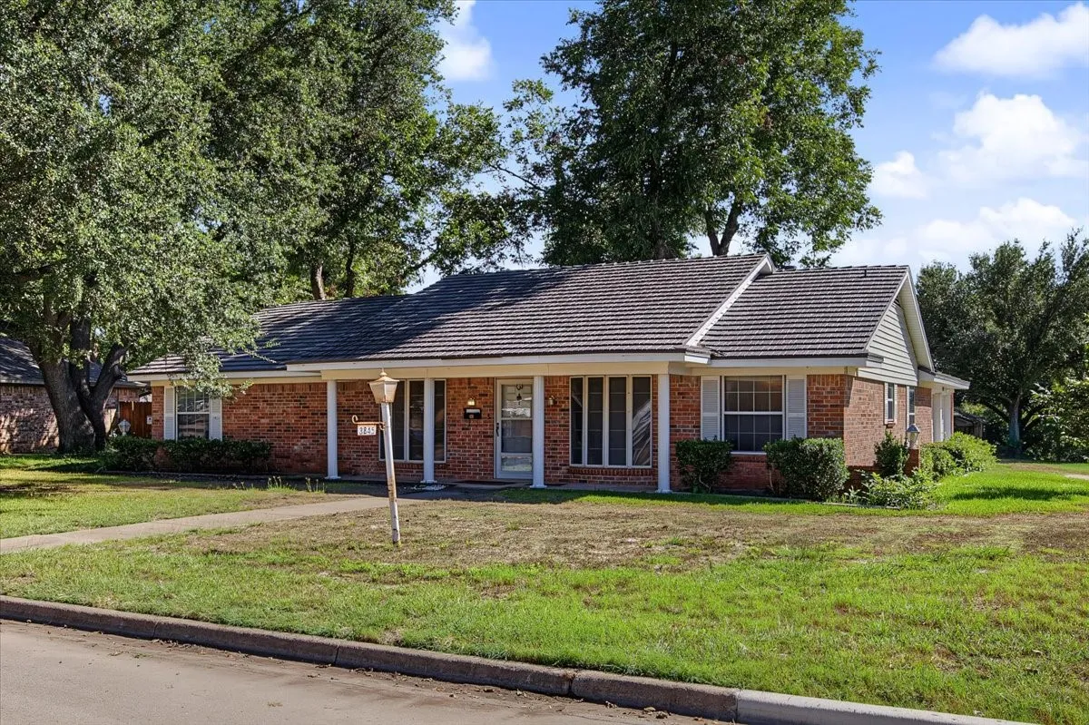 Brick exterior with white columns and shutters, mature trees, and a walkway