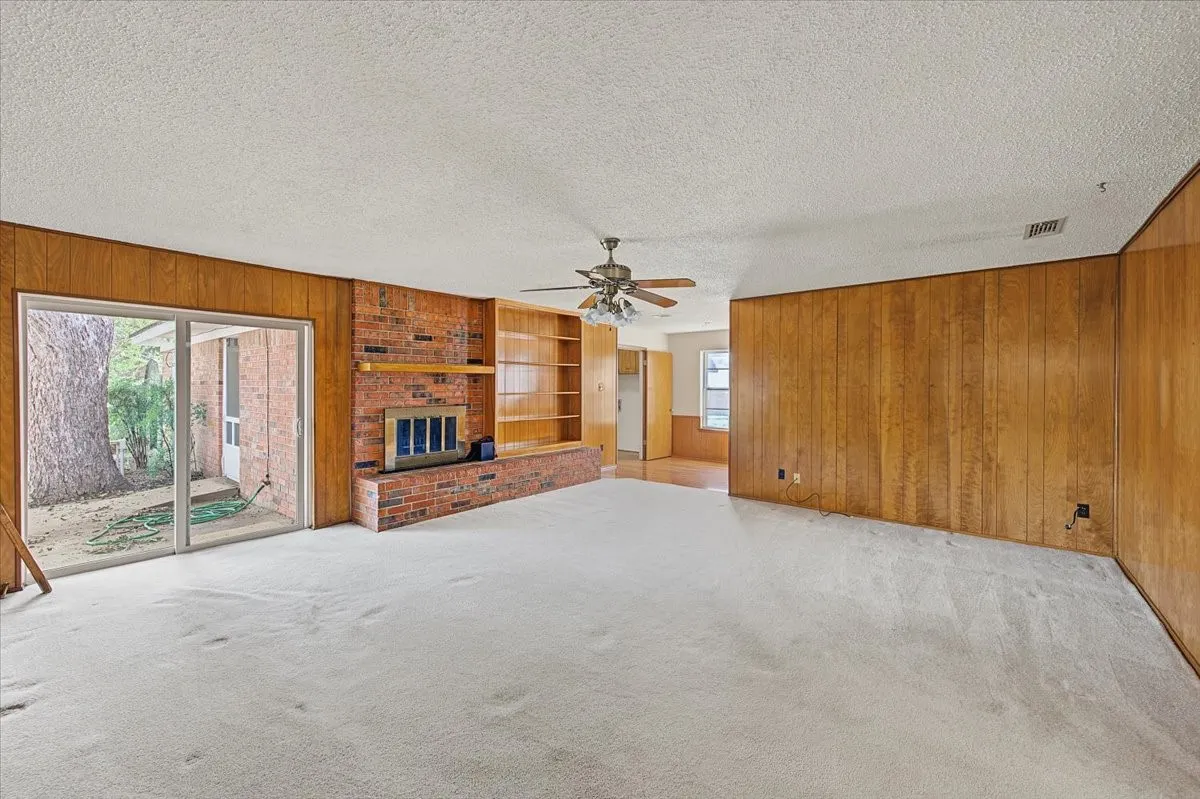 Spacious living area featuring a brick fireplace, built-in shelving, wood-paneled walls, and sliding glass doors