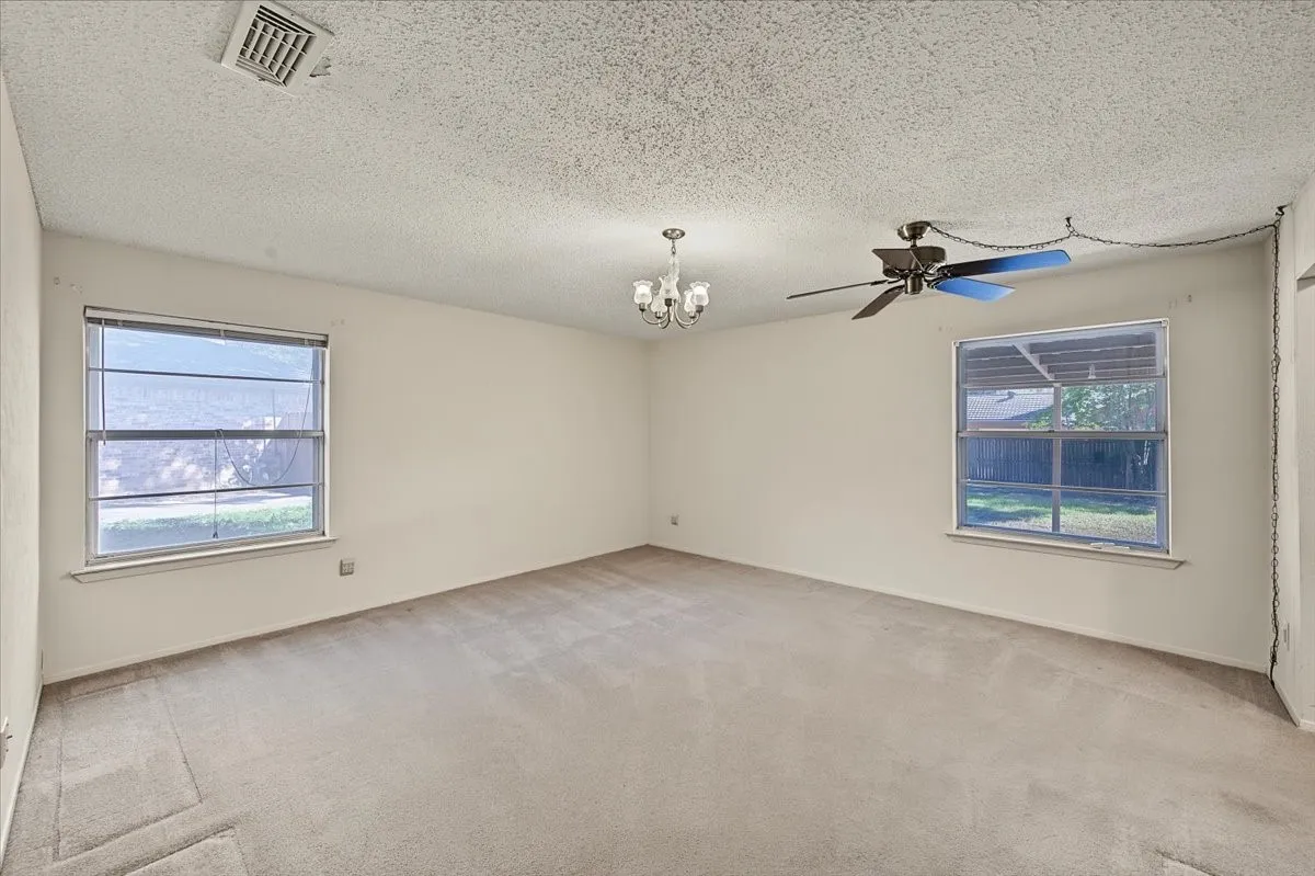 Neutral wall paint with two windows, a ceiling fan, and a chandelier