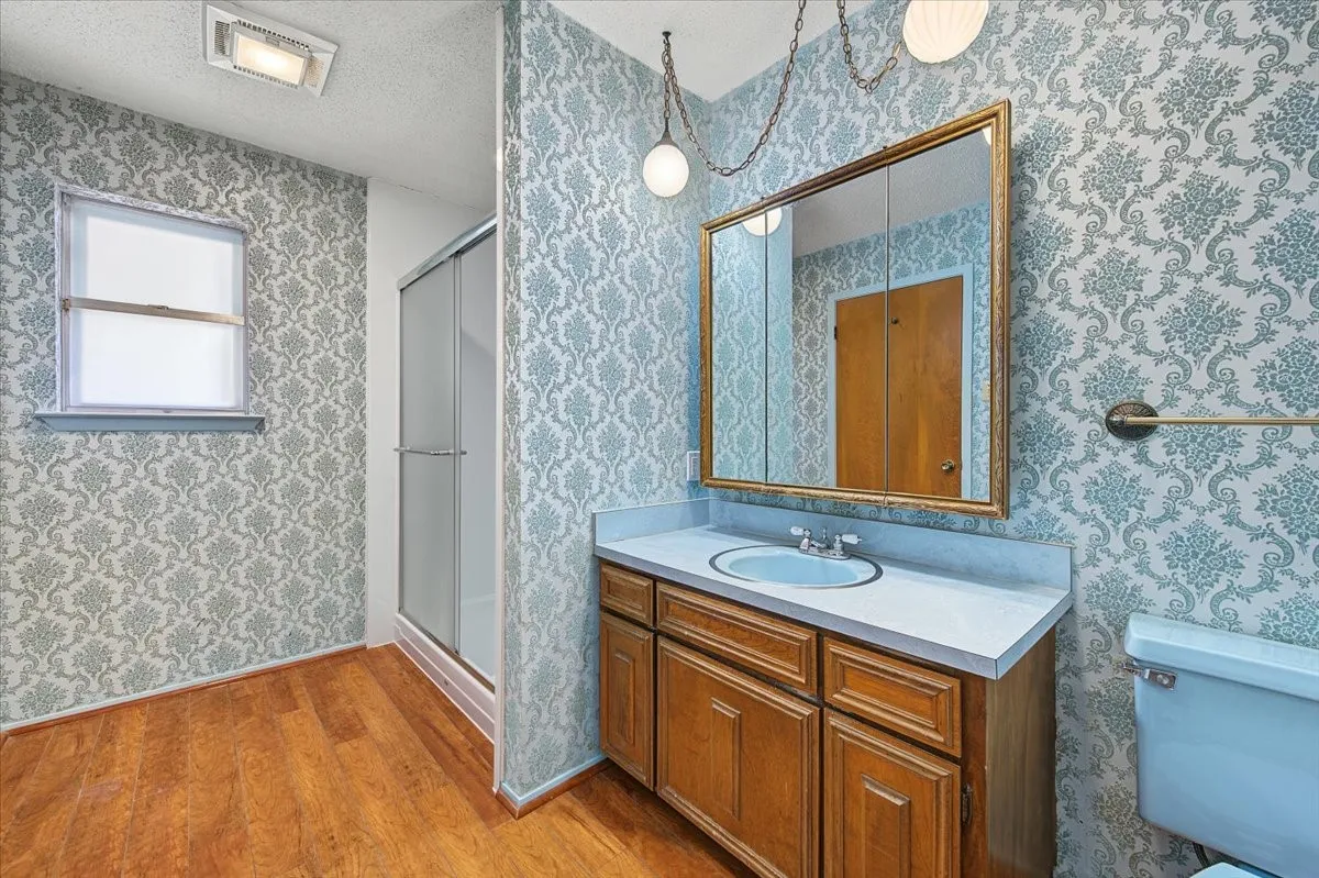 Wood-finish flooring, single vanity with integrated sink, framed mirrored medicine cabinet, enclosed shower, and window