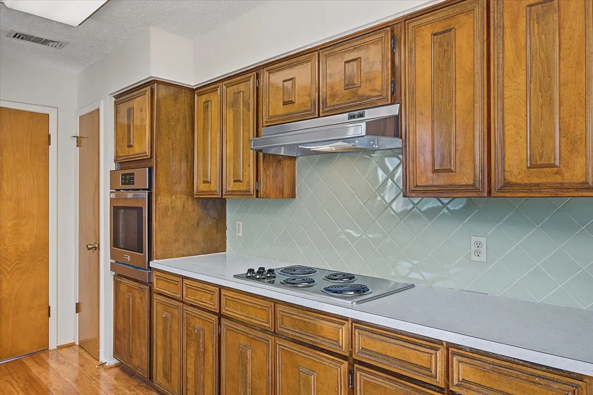 Kitchen featuring wood cabinetry, stainless steel wall oven, light-toned countertops, and a tiled backsplash