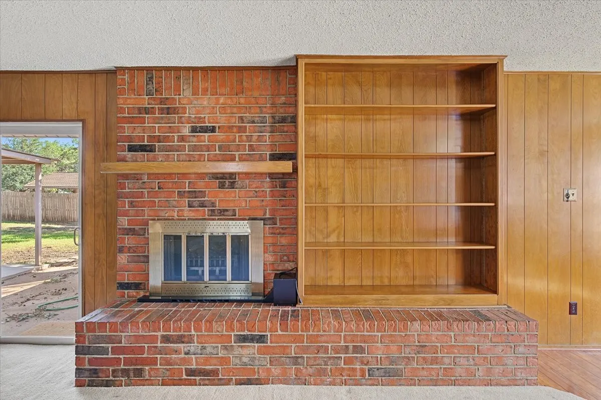 Brick fireplace with a wood mantle, built-in shelving, and wood paneling