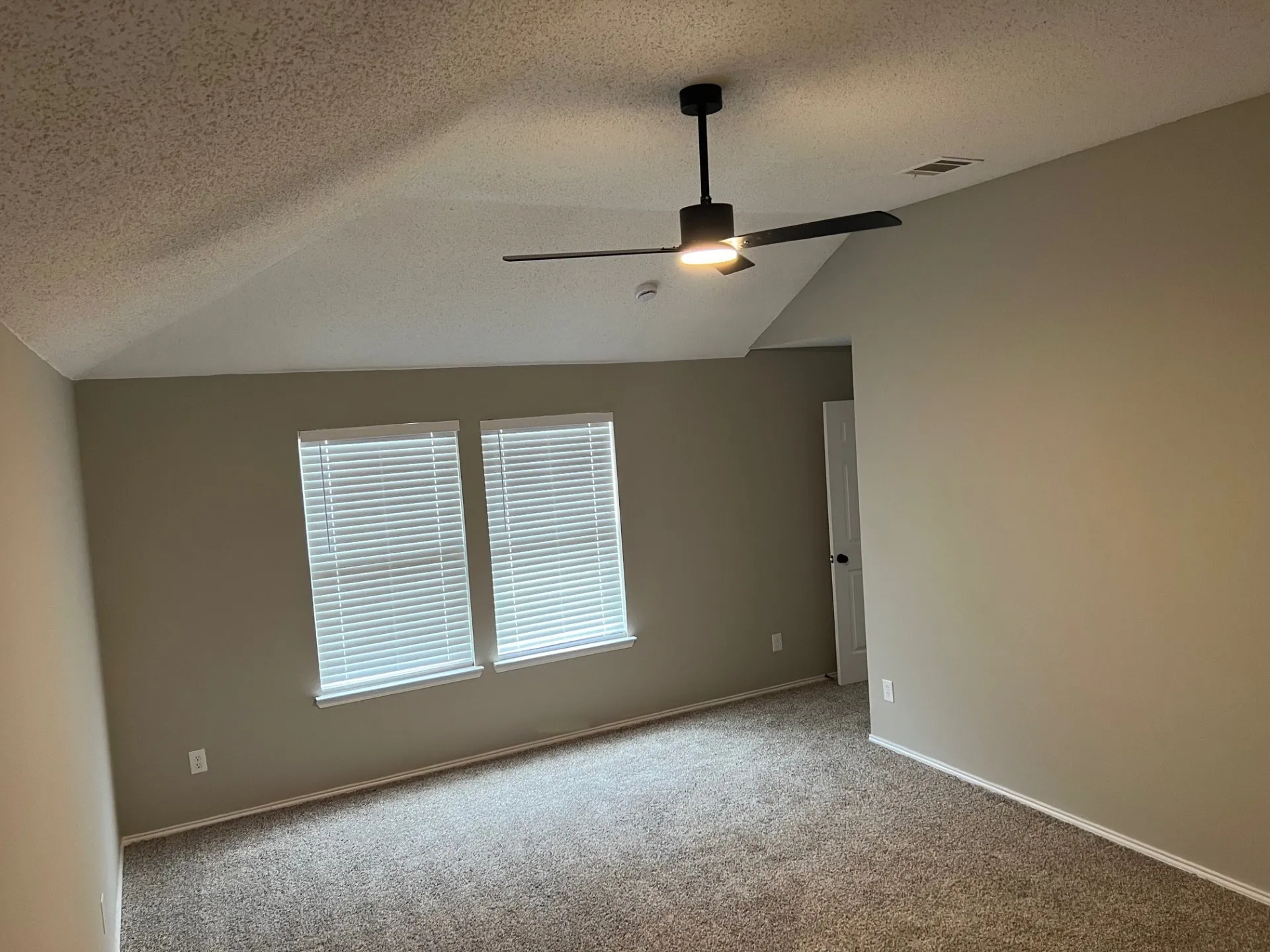 Vaulted ceiling featuring a contemporary ceiling fan with integrated lighting, textured wall finish, and two windows with blinds