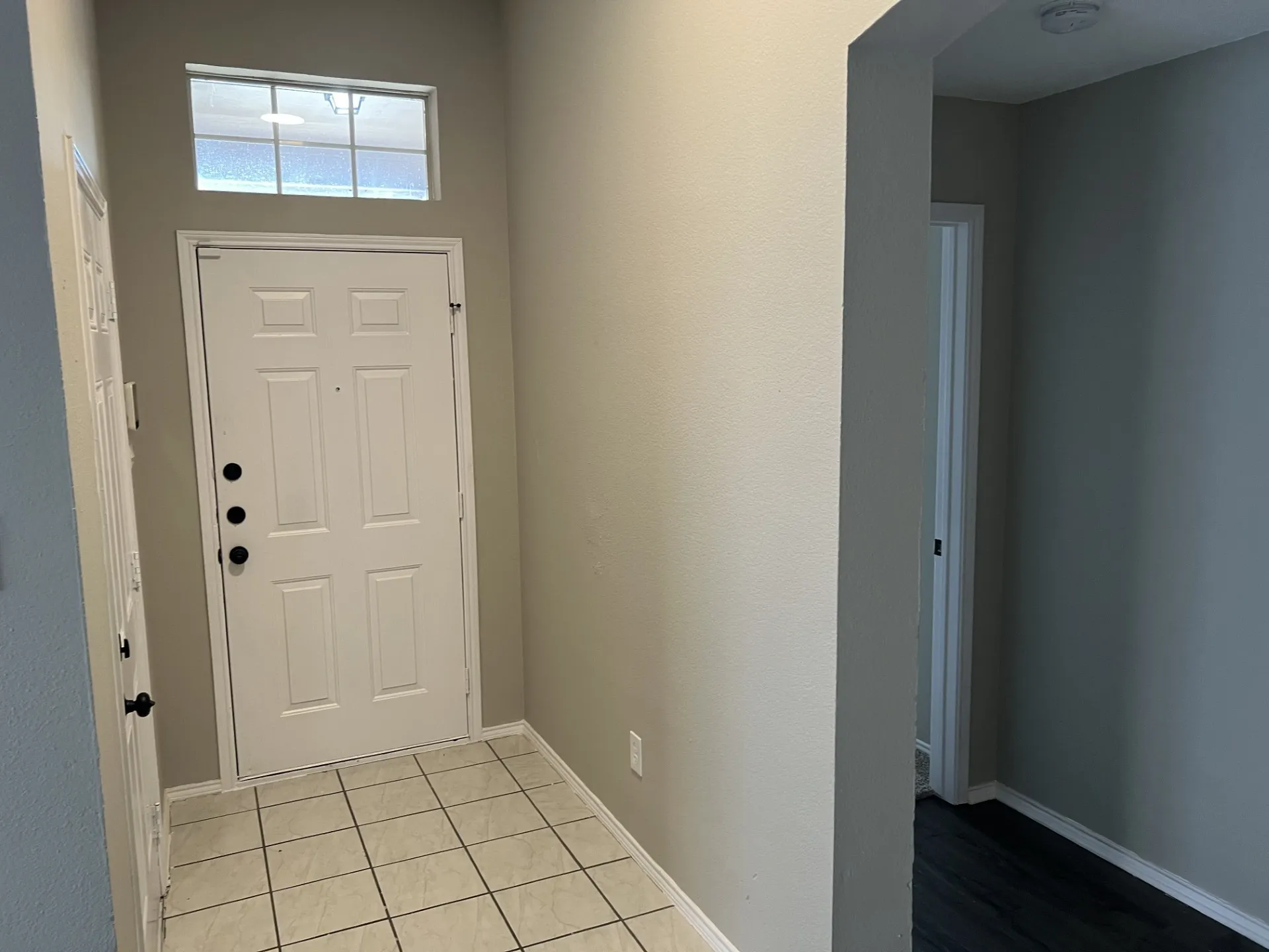Entryway featuring a paneled door with black hardware, transom window, and tile flooring