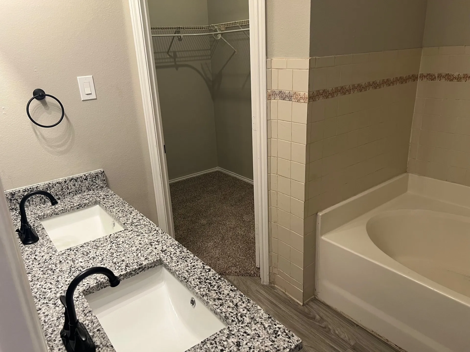 Dual vanity with granite-style countertop and integrated sinks, matte black faucets, and wood-finish flooring