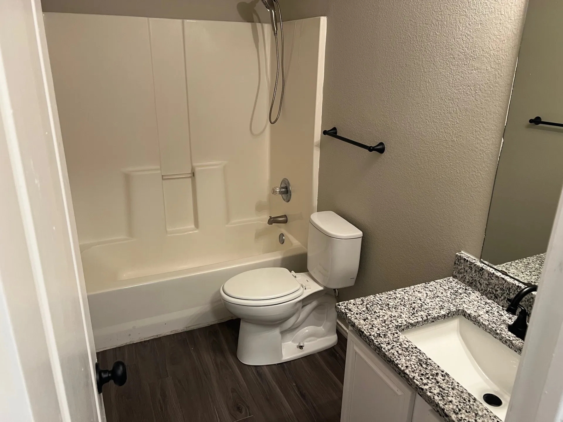 Bathroom featuring a full-size tub with shower, wood-finish flooring, a vanity with a granular countertop, and a built-in mirror