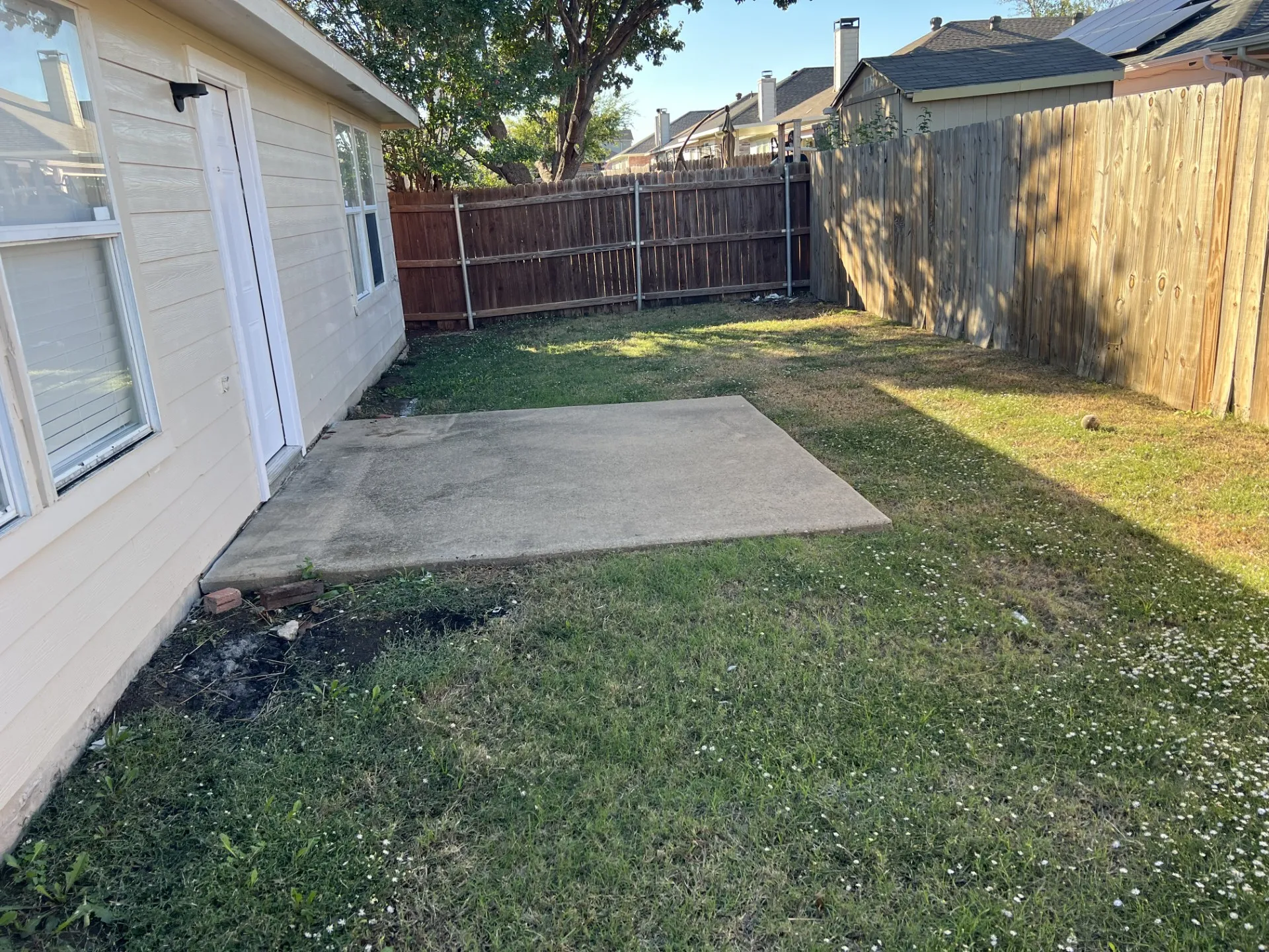 Spacious backyard featuring a concrete patio, mature shade trees, and well-established lawn area