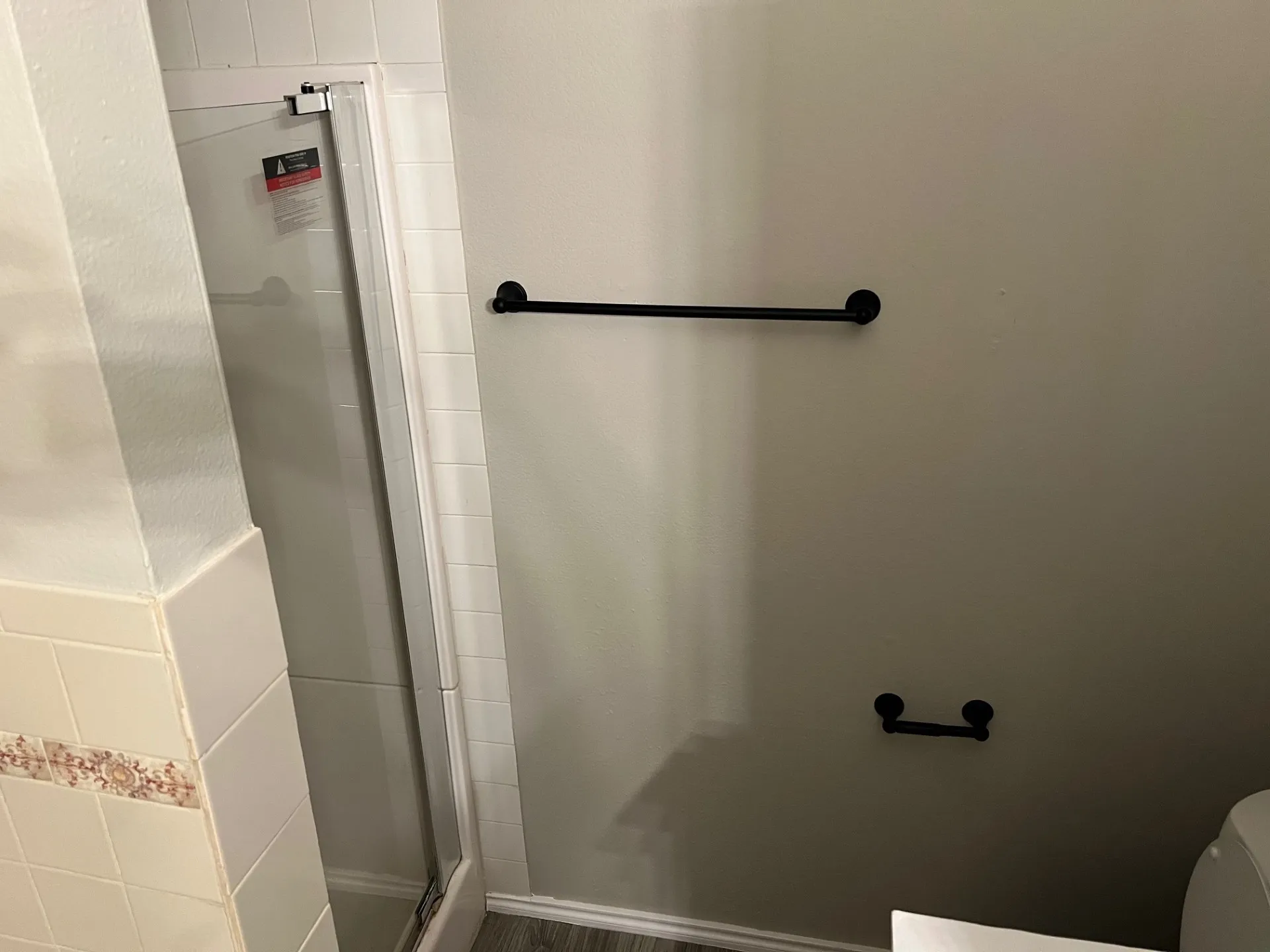 Shower enclosure with clear glass panel, matte black towel bar, and coordinating matte black toilet paper holder