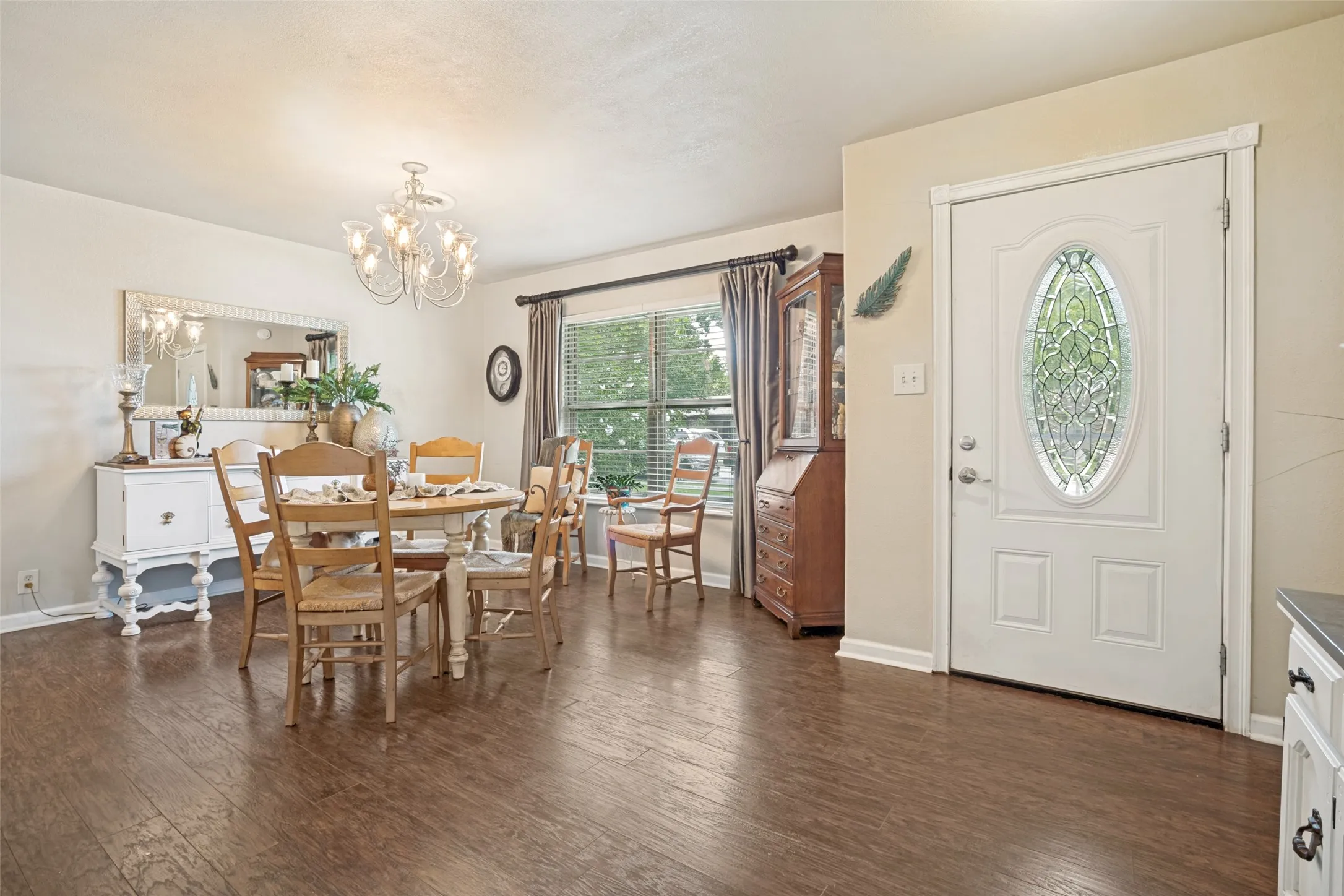 Wood-like flooring, white panel door with decorative oval glass insert, and a window with blinds