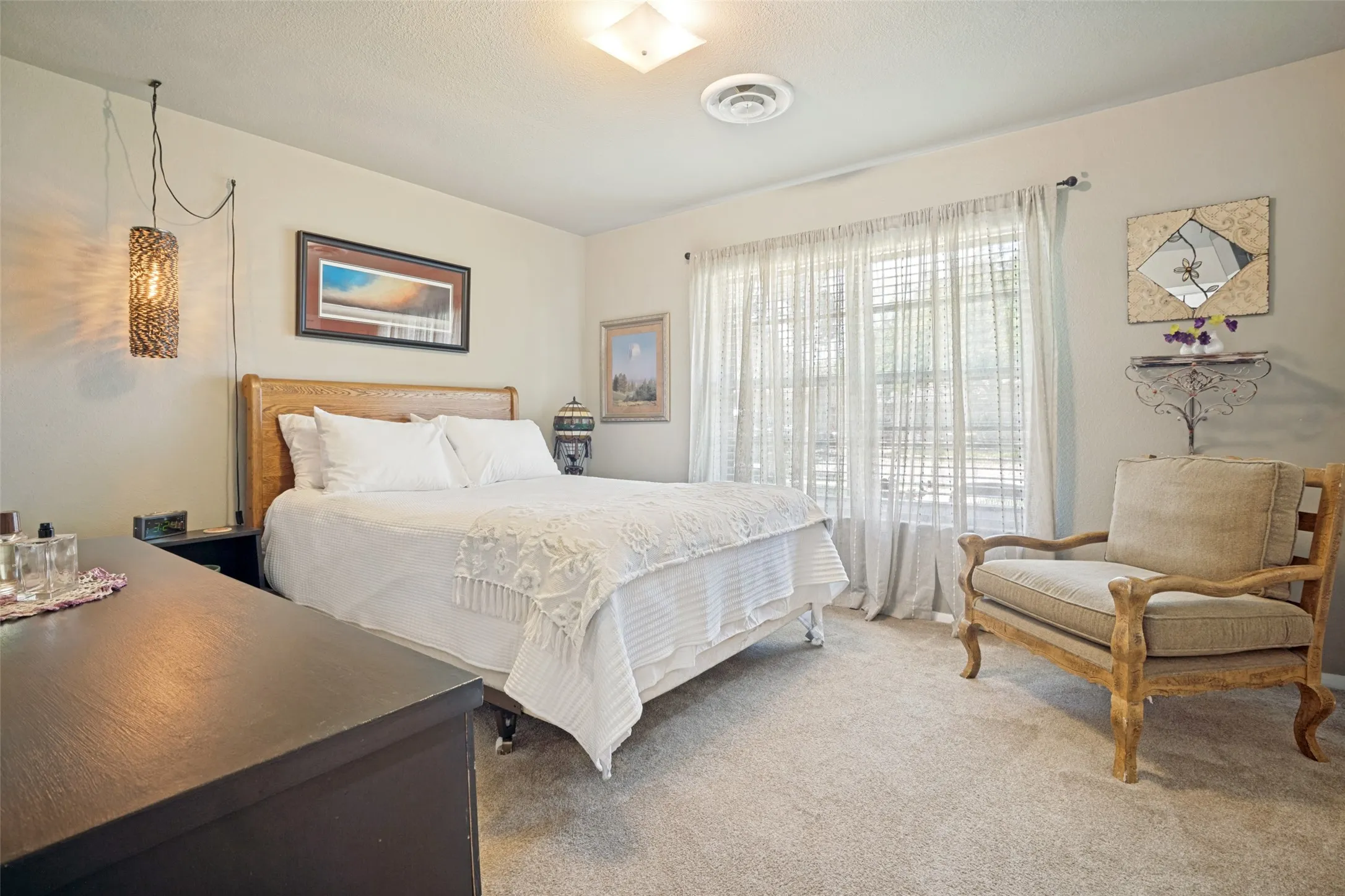 Recessed ceiling light, suspended sconce light, window with white sheers, built-in shelving, and light-colored carpeting