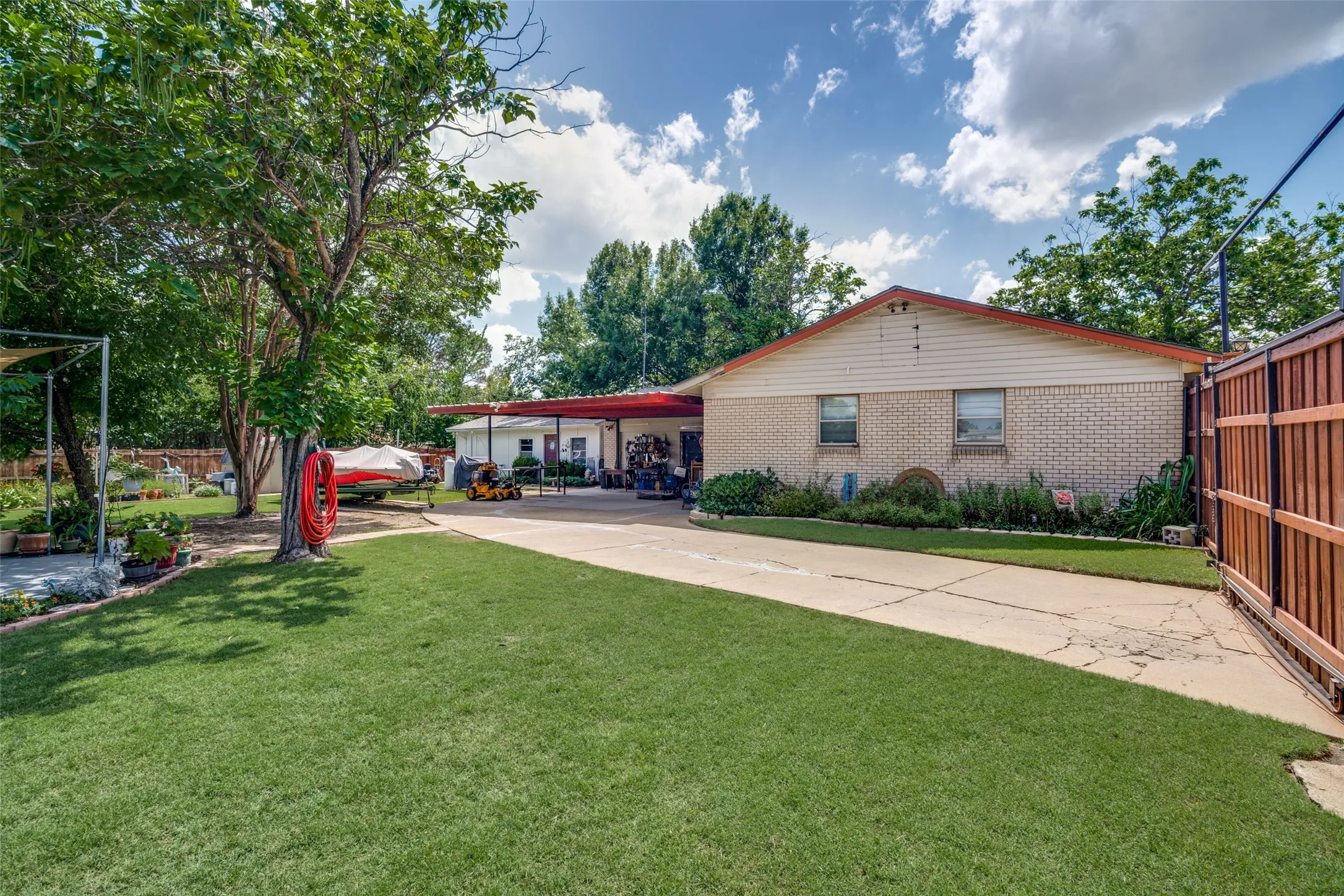 Expansive concrete driveway, mature landscaping, and a privacy fence