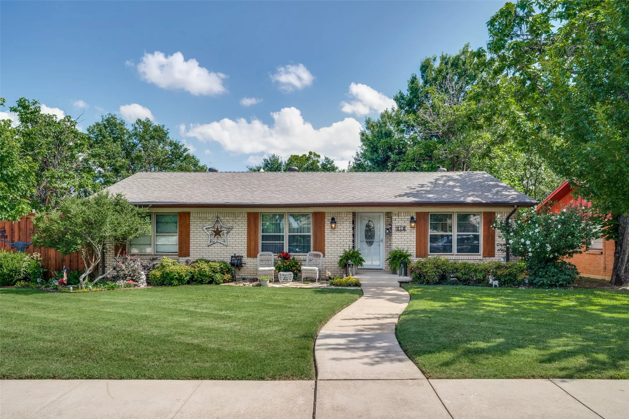 Light brick exterior with wood-finish shutters, a curved concrete pathway, front porch, and mature landscaping