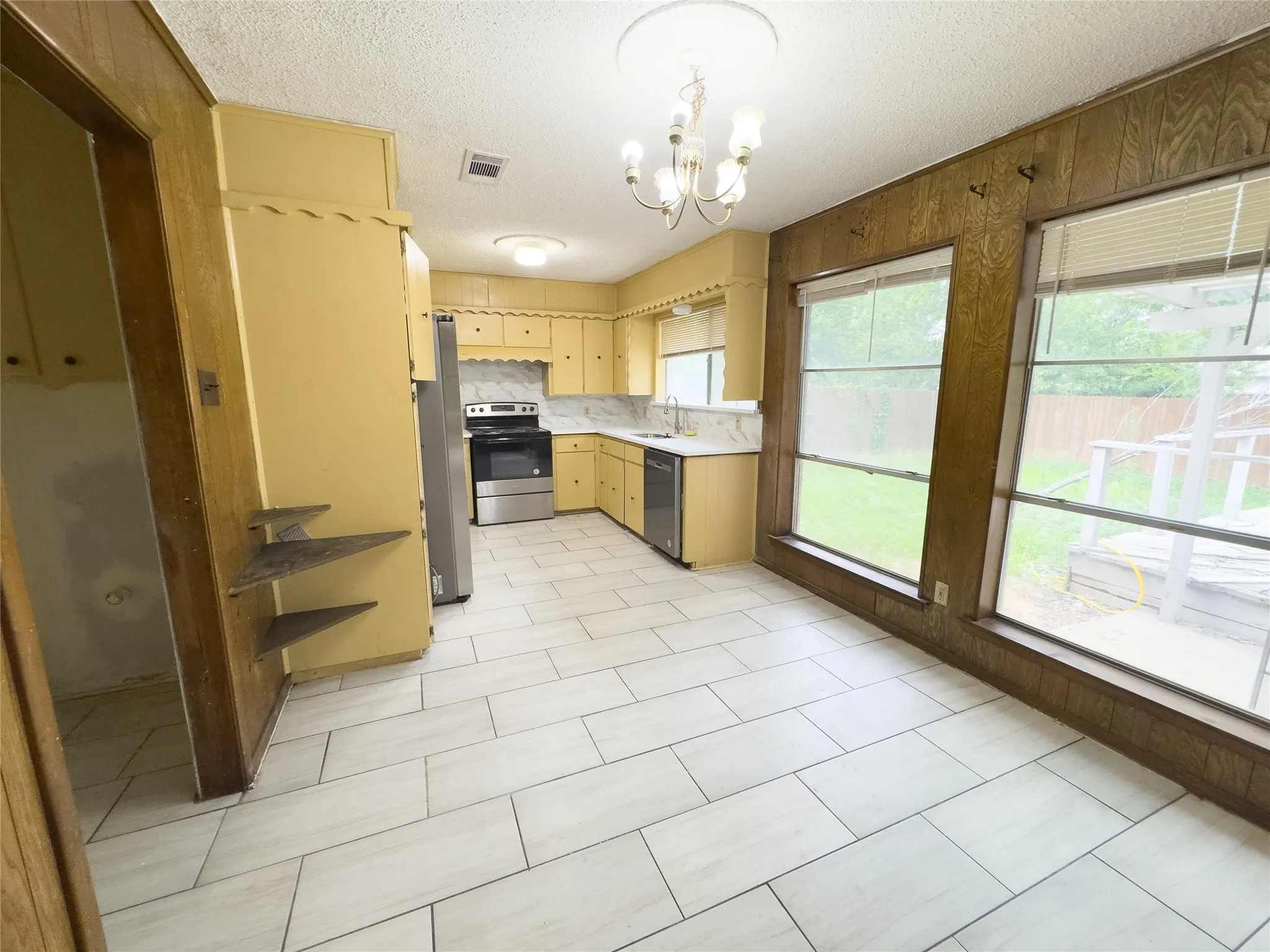 Kitchen featuring light-toned tile flooring, stainless steel appliances, corner sink with faucet, white countertops, and wood-paneled walls