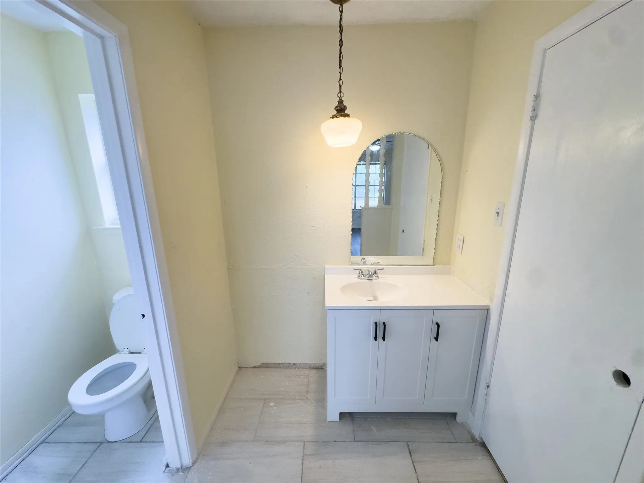 White vanity with a single basin sink, white countertop, and dark cabinet hardware