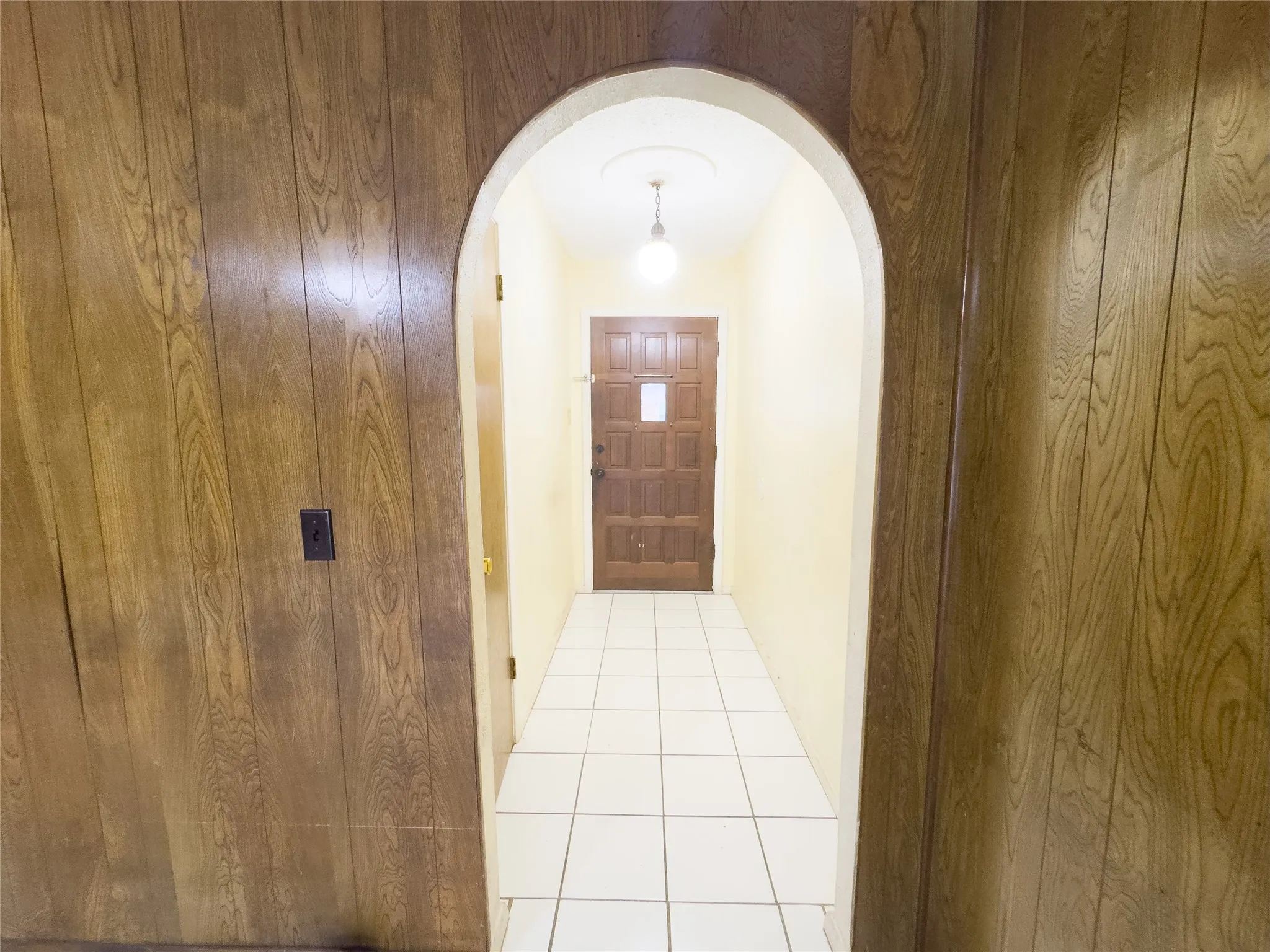 Wood-finish wall paneling, arched doorway, recessed ceiling light, paneled door, ceramic tile flooring