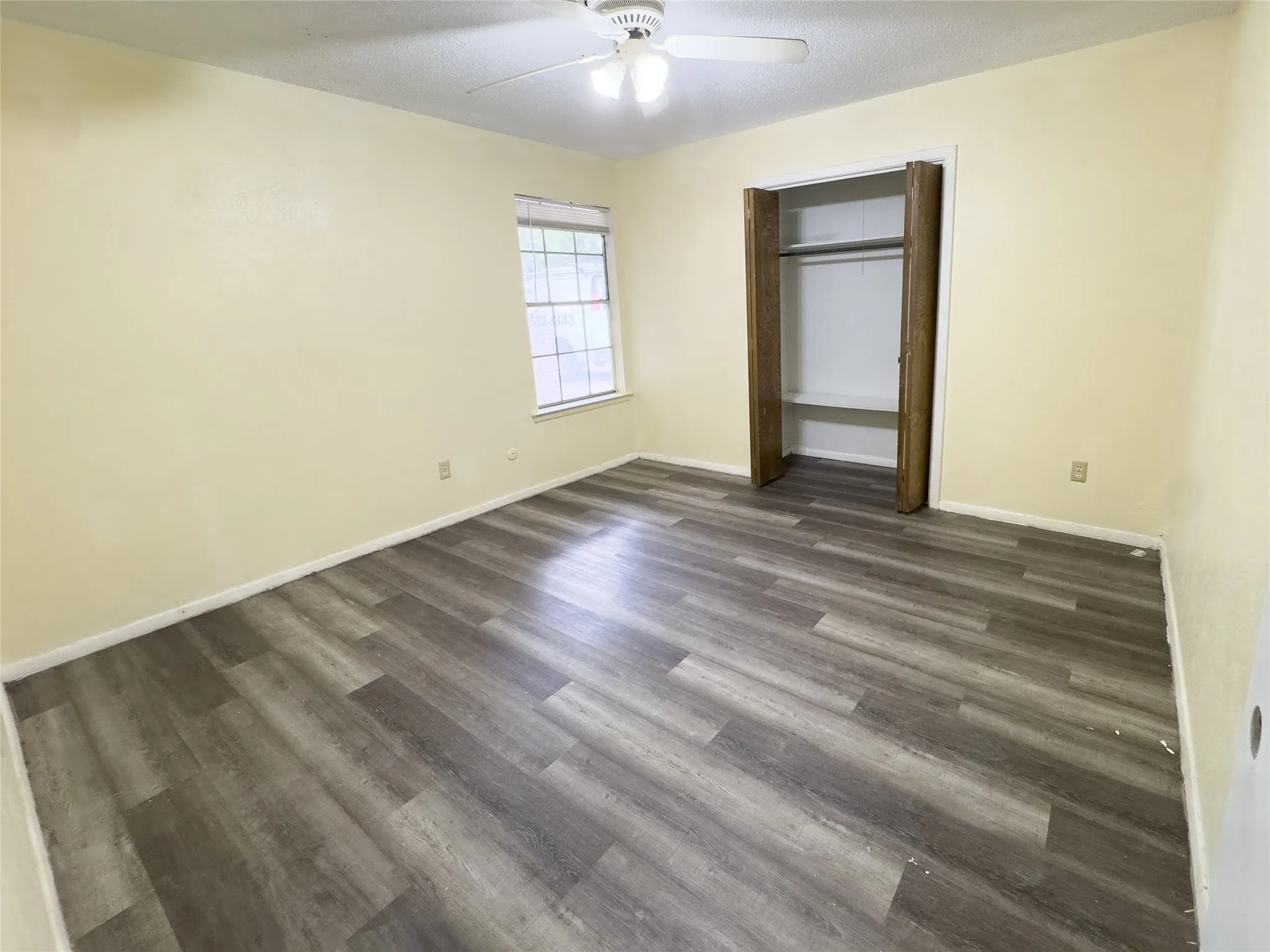 Wood-finish flooring throughout, bright window, ceiling fan with light fixture, and an open closet with shelving