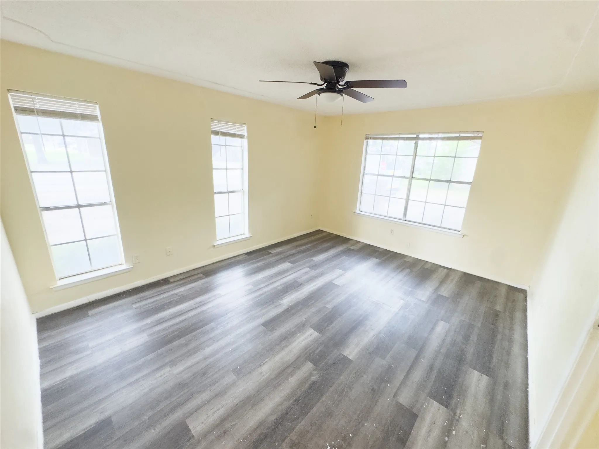 Spacious room featuring wood-finish flooring, multiple windows, and a ceiling fan