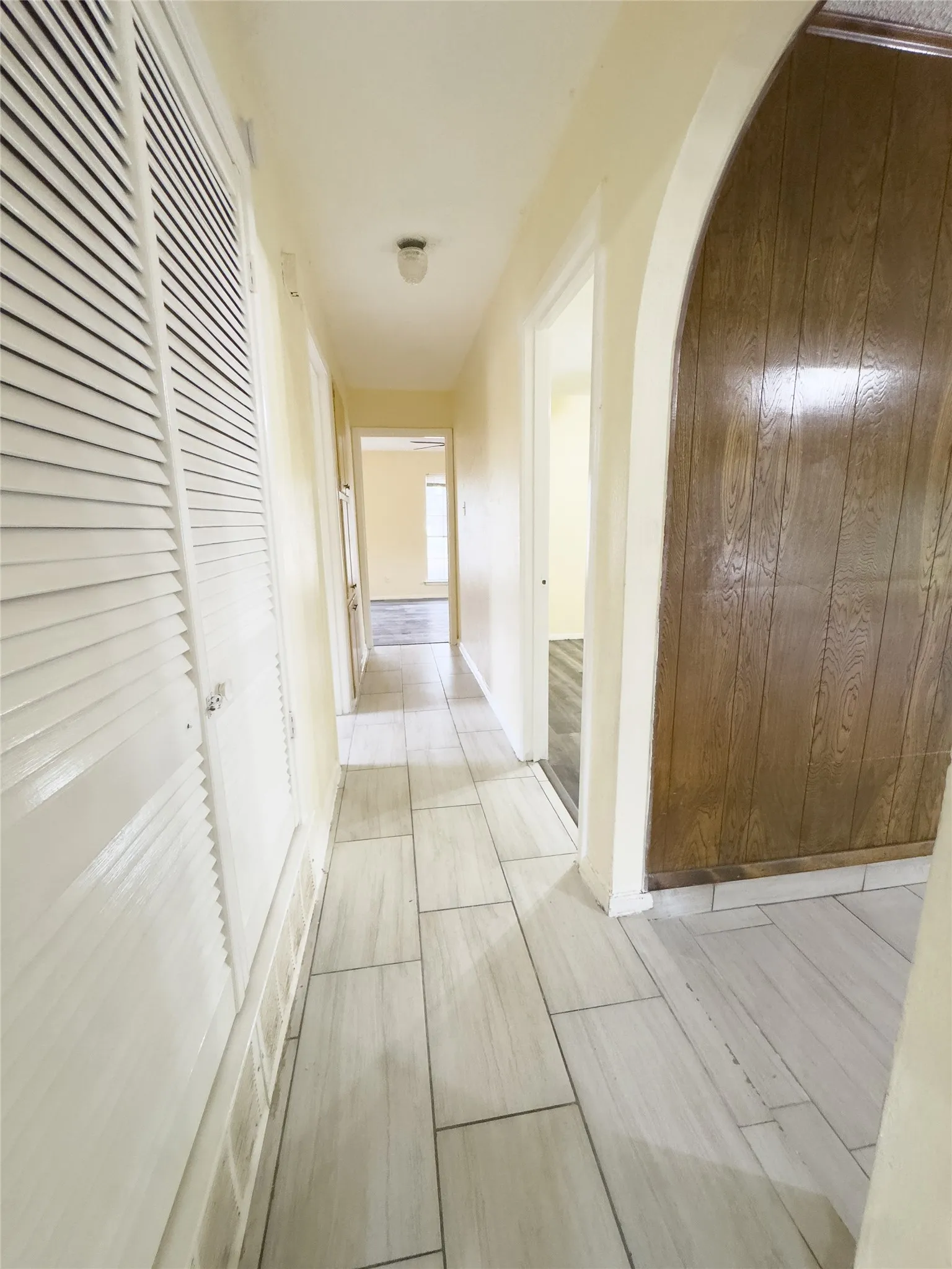 Light-toned tile flooring, louvered utility doors, and an arched entry feature within a corridor