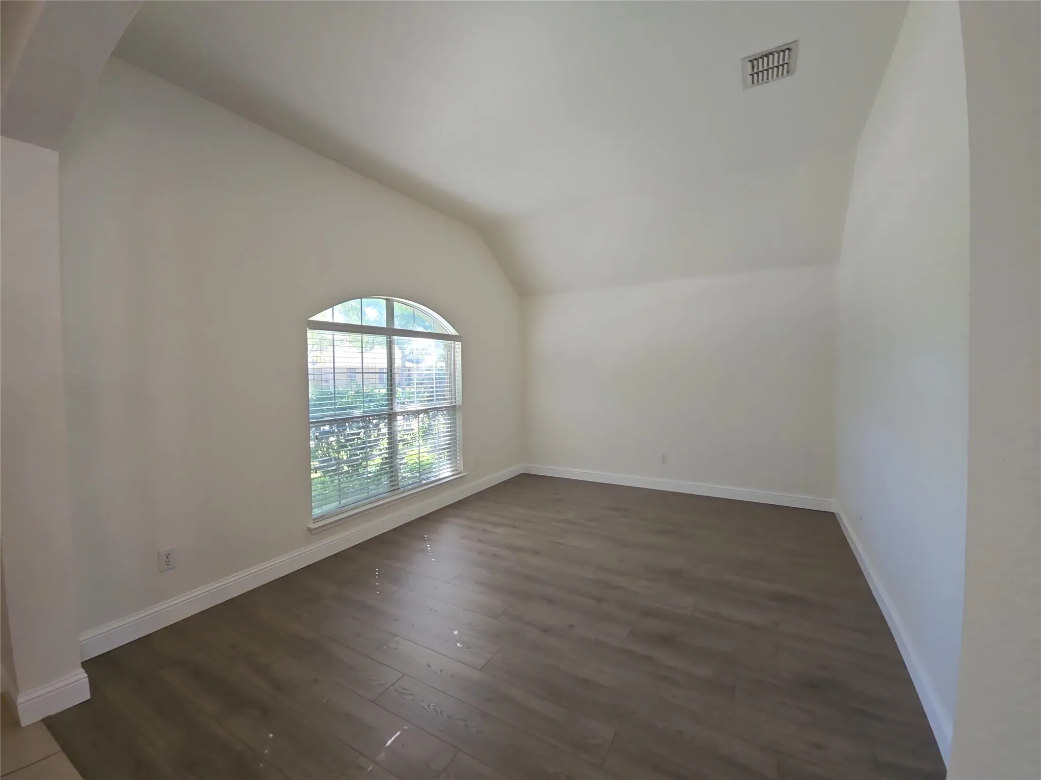 Vaulted ceiling room featuring wood-finish flooring and an arched window with blinds