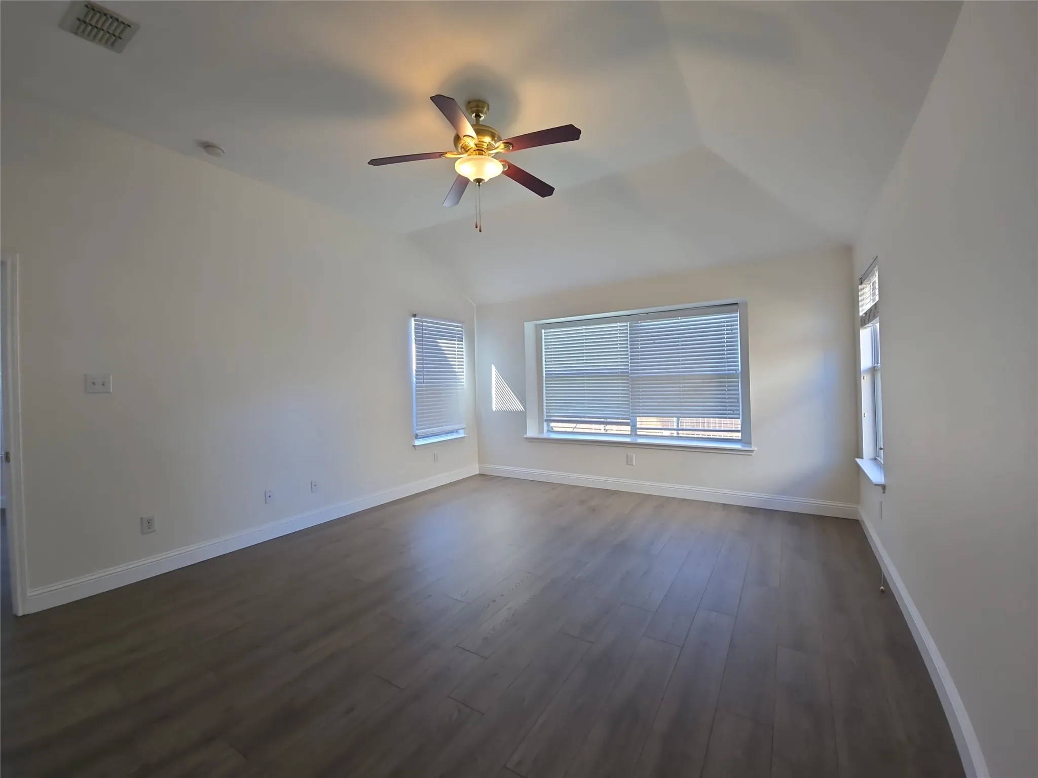 Vaulted ceiling with a ceiling fan, multiple windows with blinds, and wood-finish flooring