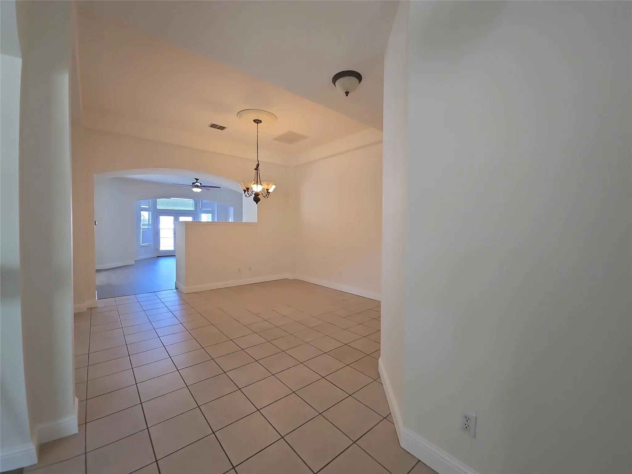 Tiled flooring, arched entryway, tray ceiling with decorative medallion, and a chandelier lighting fixture