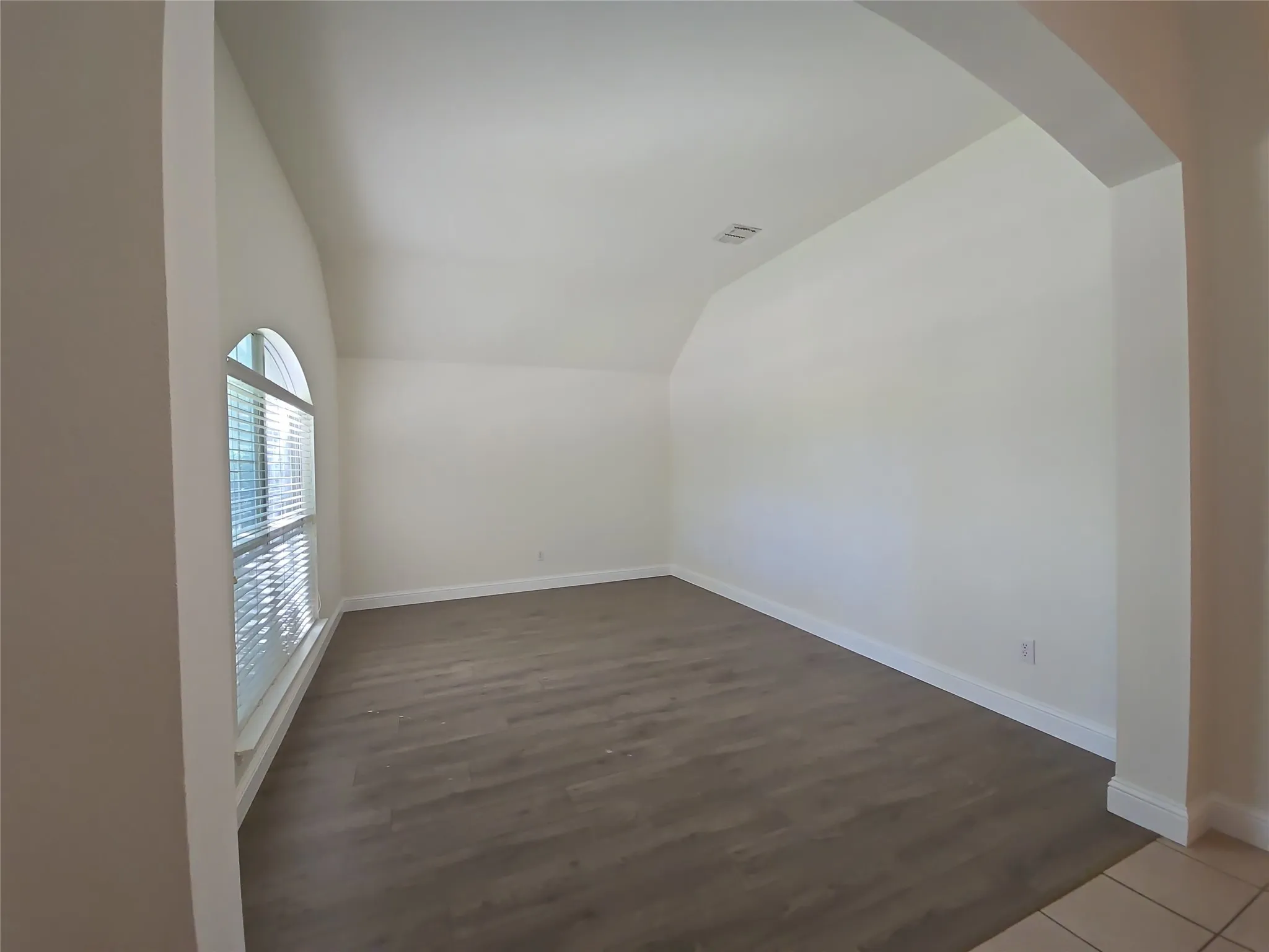 Arch window with blind, wood-finish flooring, vaulted ceiling, and an arched entry