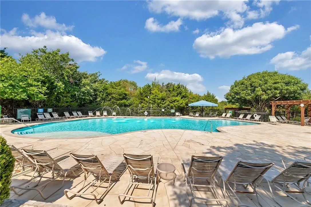 Expansive resort-style swimming pool featuring water fountains, a surrounding stone paver deck, and a shaded pergola area