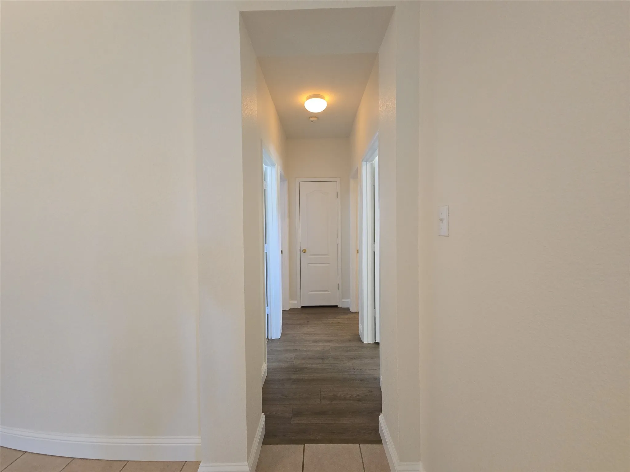 Hallway with wood-finish flooring, light-colored walls, and a ceiling-mounted light fixture