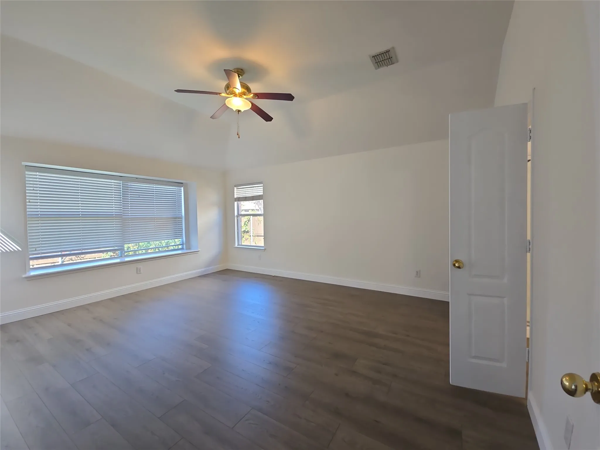 Vaulted ceiling, wood-finish flooring, ceiling fan with integrated lighting, multiple windows with blinds, and a paneled interior door