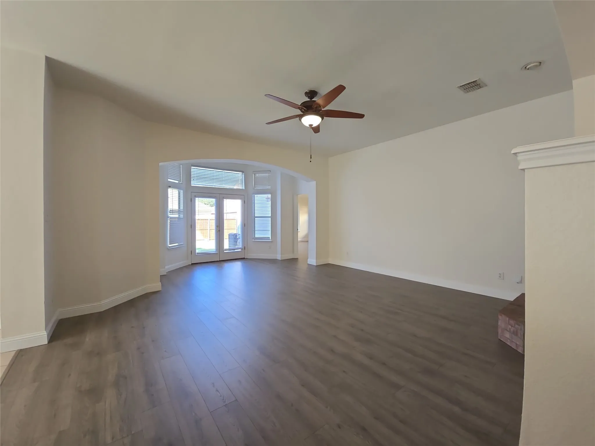 Spacious living area featuring wood-finish flooring, an arched doorway, and a ceiling fan