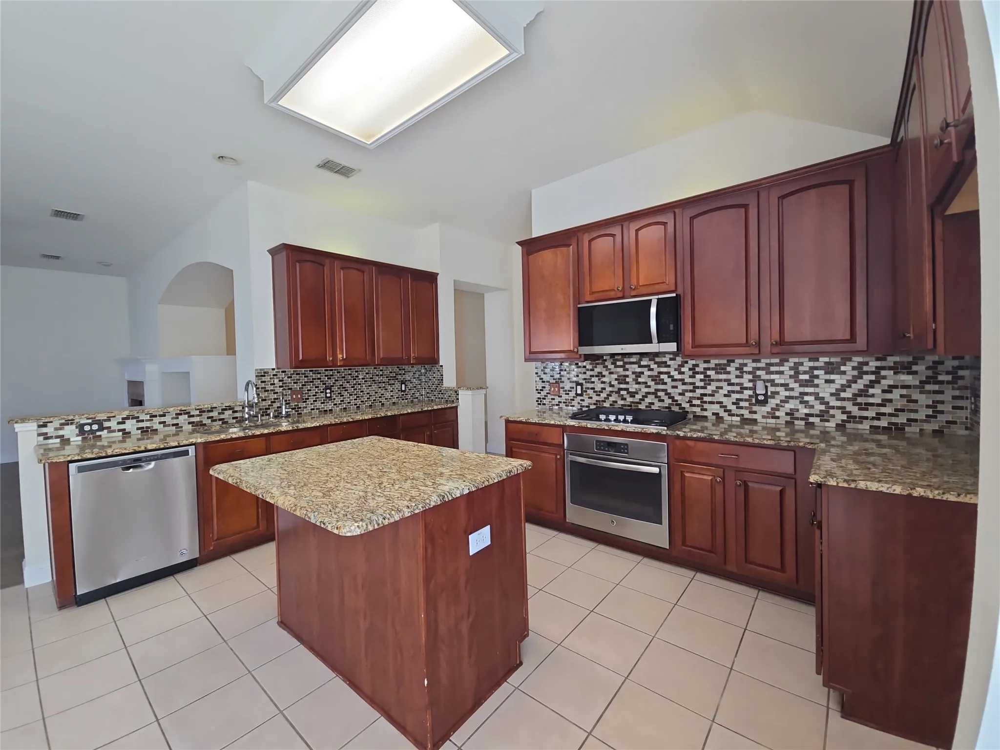 Kitchen featuring rich wood cabinetry, stainless steel appliances, granite countertops, and a mosaic tile backsplash