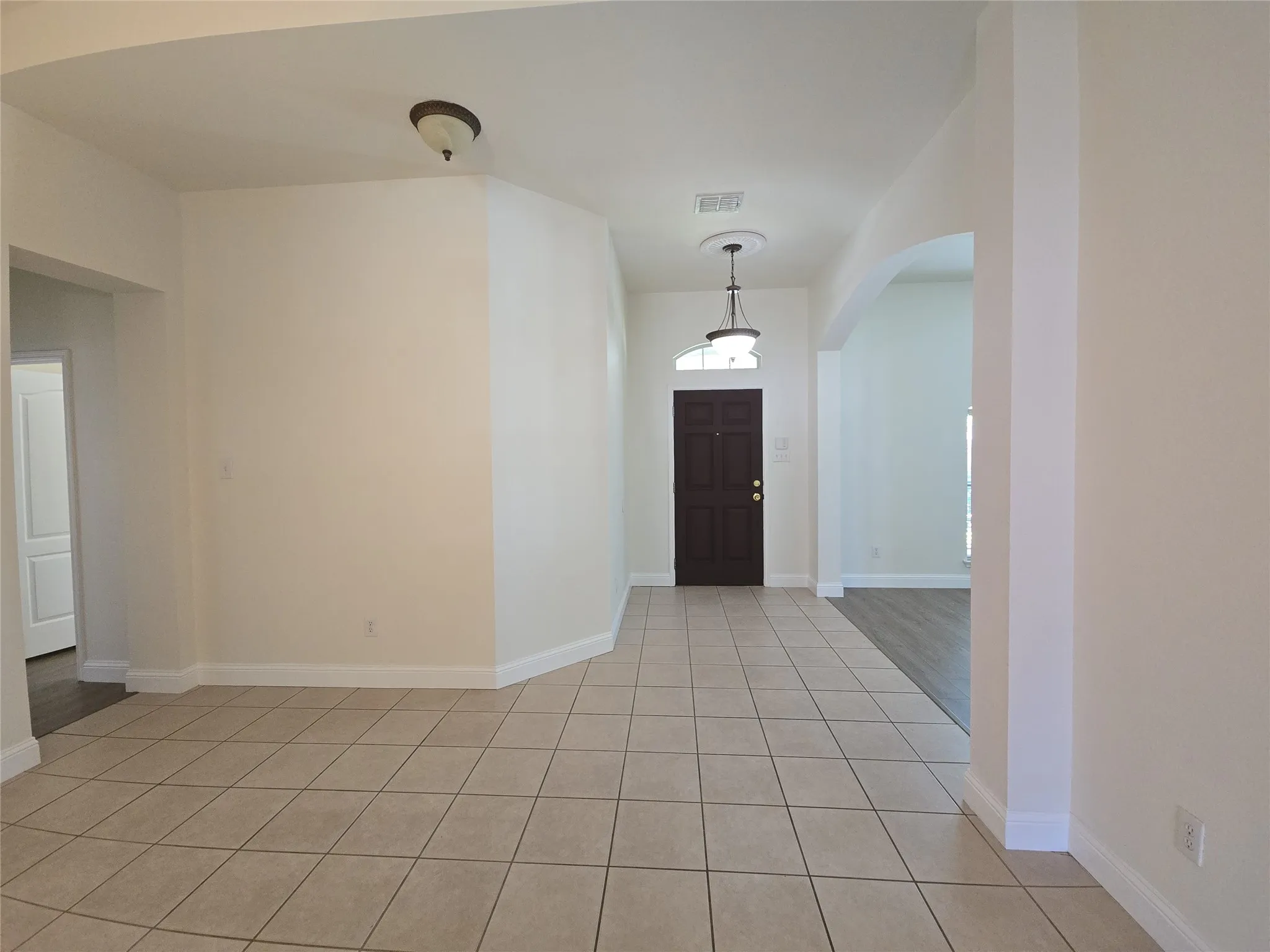 Entryway featuring a dark wood-finish door with an arched transom, tile flooring, archway detailing, and a decorative pendant light fixture