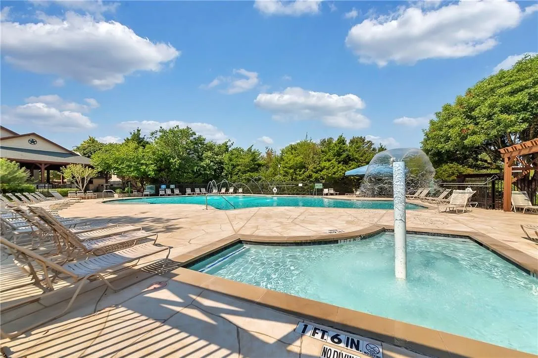 Swimming pool with integrated spa and water feature, expansive paved decking, and lush surrounding landscaping