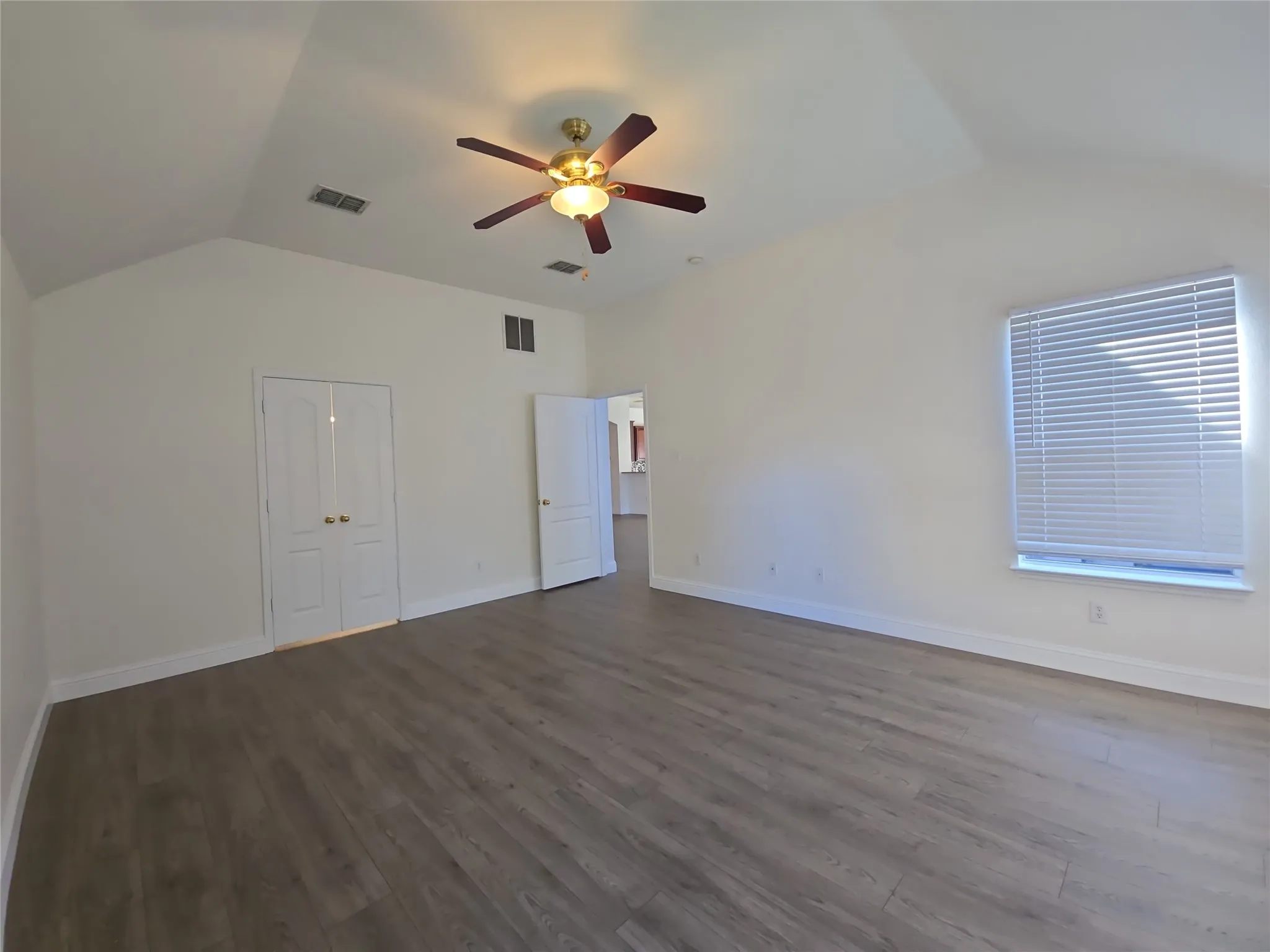 Vaulted ceiling with a ceiling fan, wood-finish flooring, white double doors, and a window with blinds