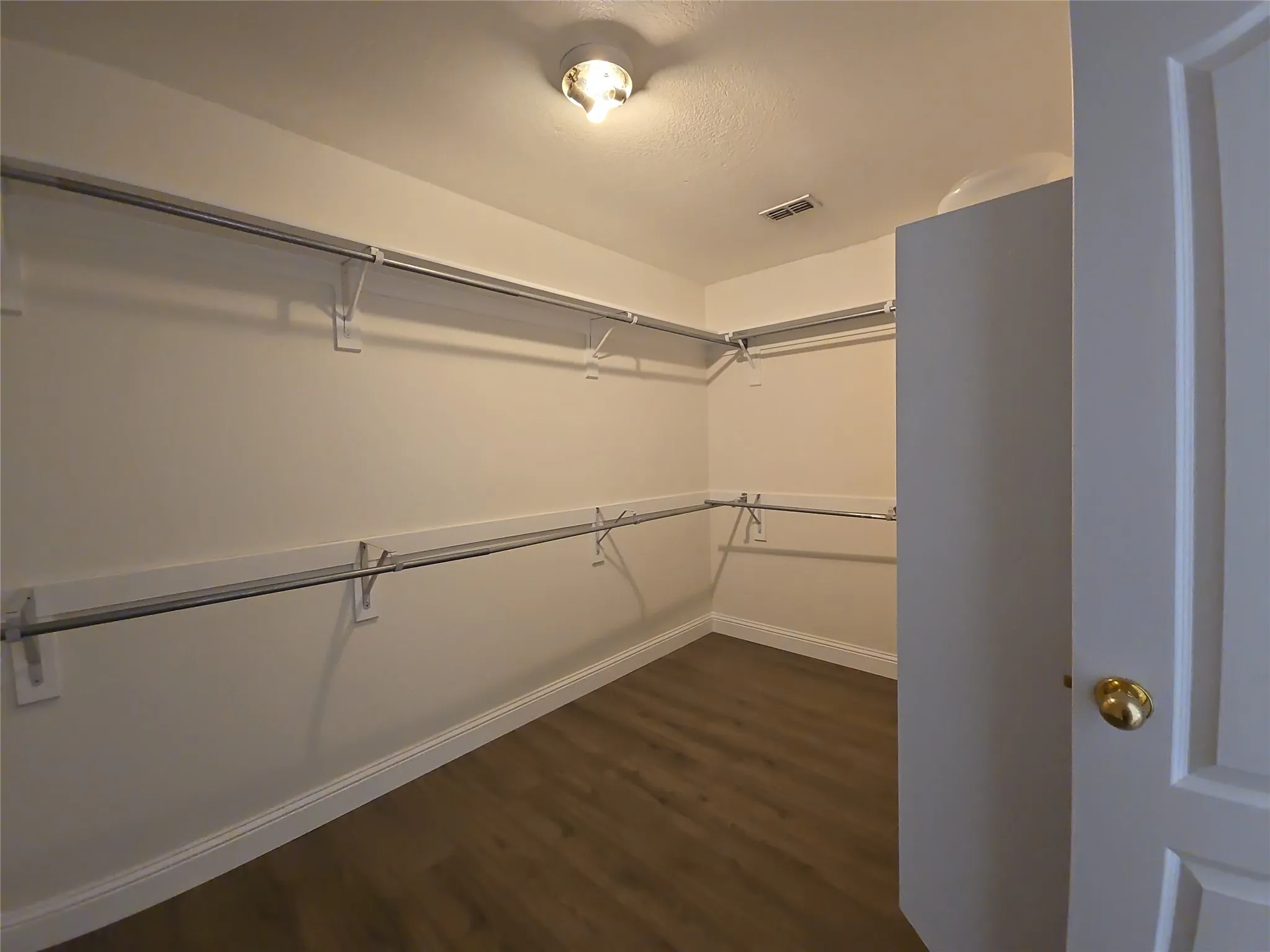 Spacious walk-in closet with wood-finish flooring, extensive built-in shelving, and hanging rods