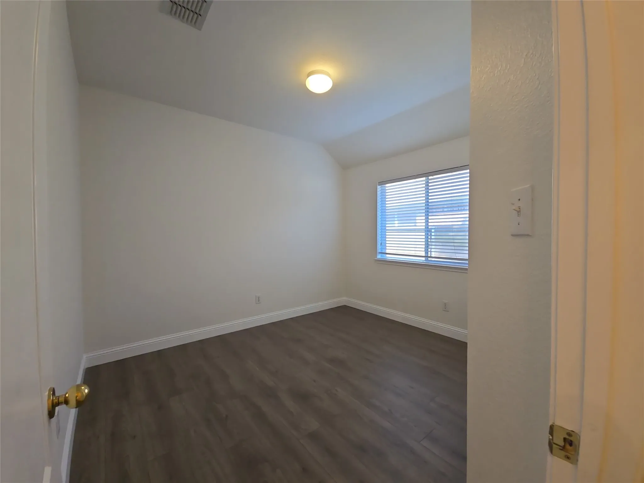 Wood-finish flooring with white baseboards, recessed window with horizontal blinds, and a ceiling-mounted light fixture