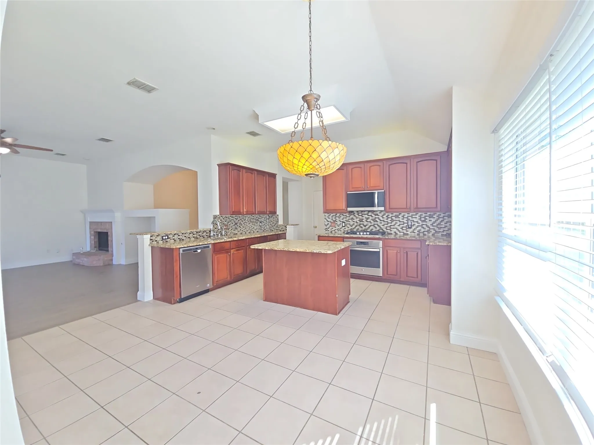 Kitchen featuring an island, integrated stainless steel appliances, wood-finish cabinetry, and granite countertops