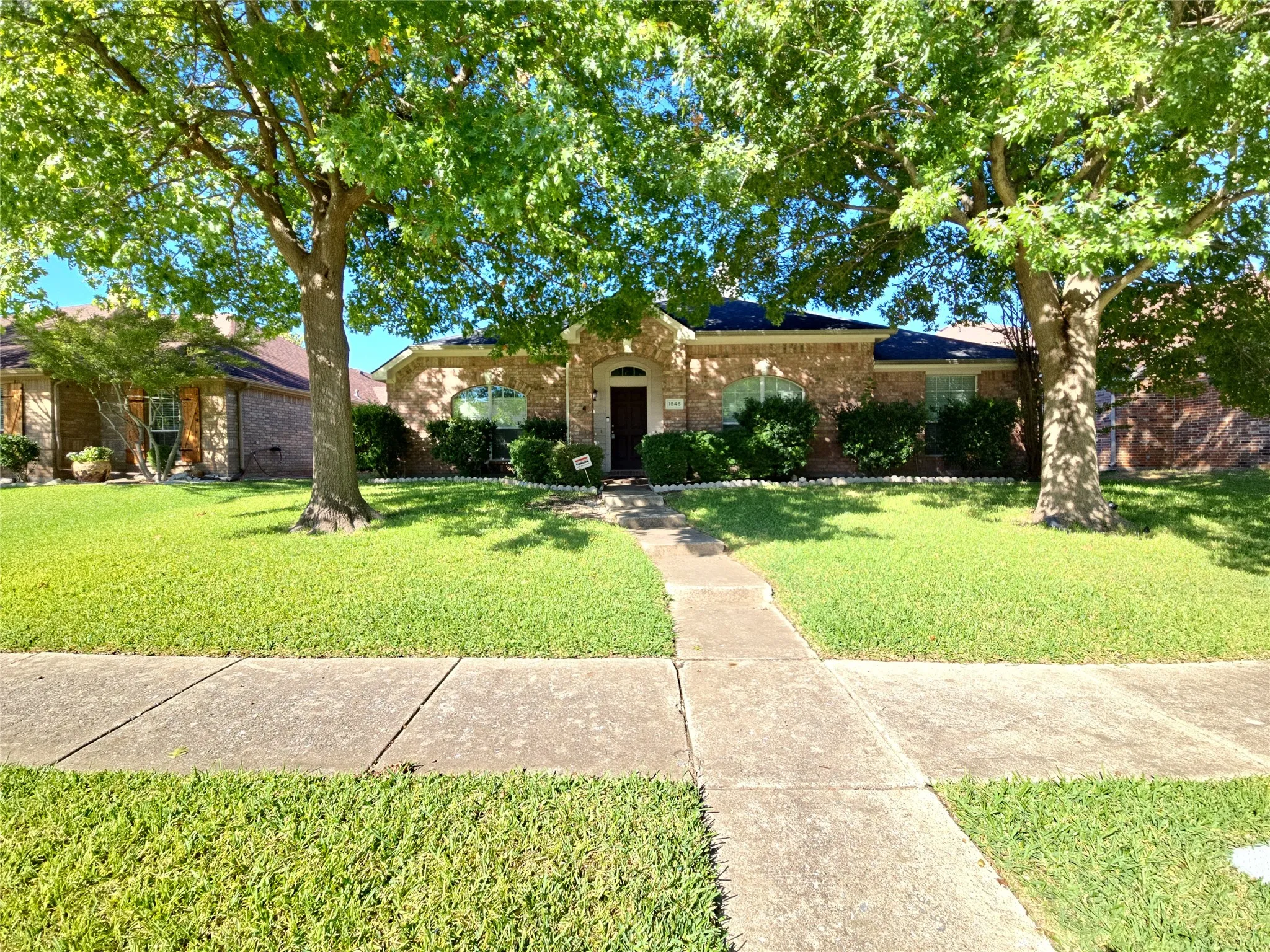 Brick exterior home with a dark shingle roof, arched windows, and a concrete pathway