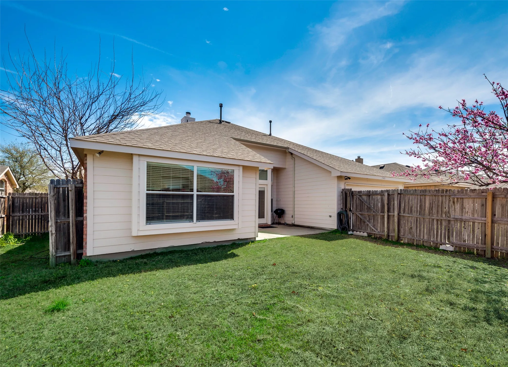 Expansive backyard featuring a manicured lawn, wood fencing, and a concrete patio
