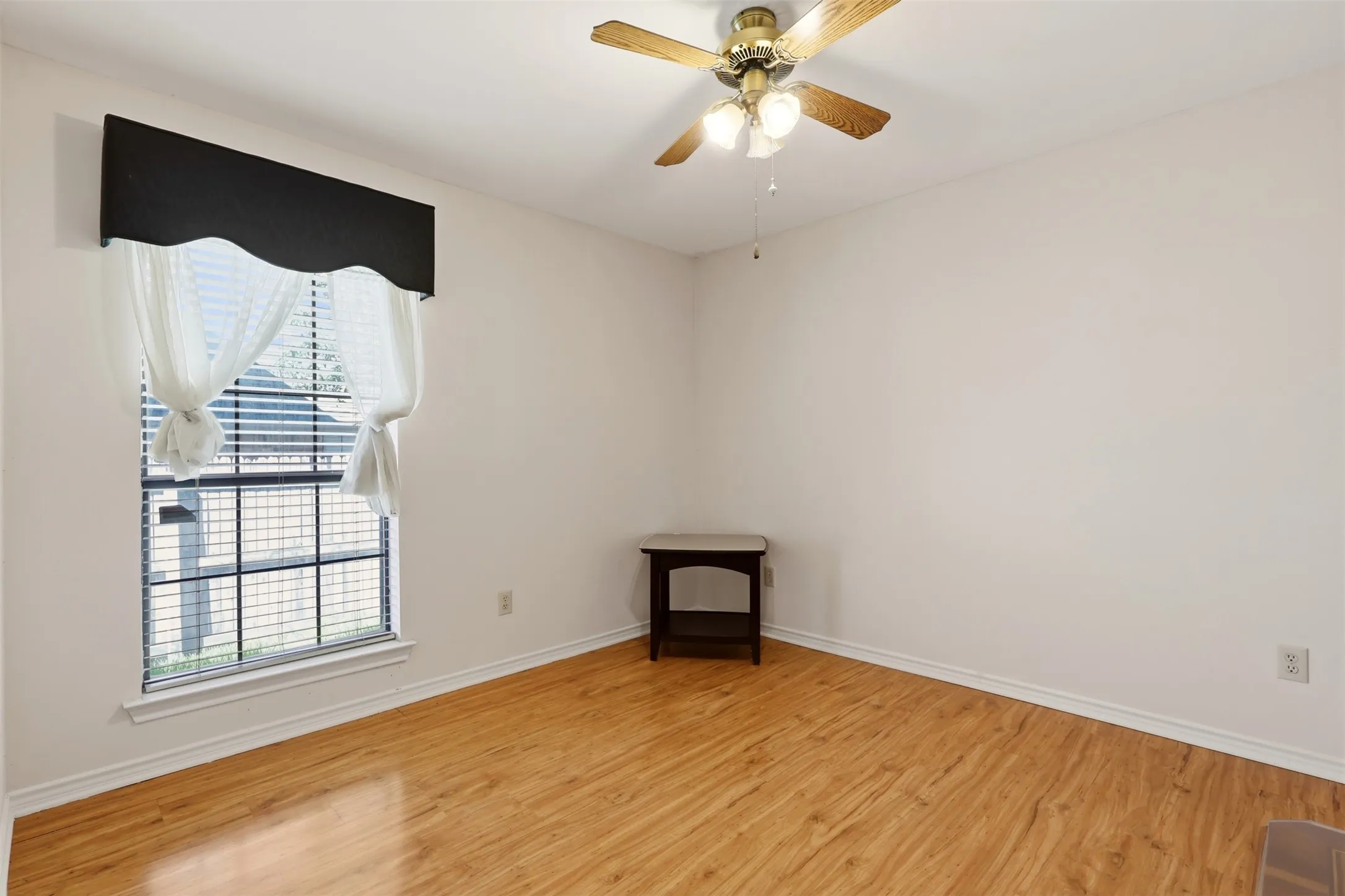 Wood-finish flooring, white painted walls, window with horizontal blinds, and a ceiling fan with light fixture