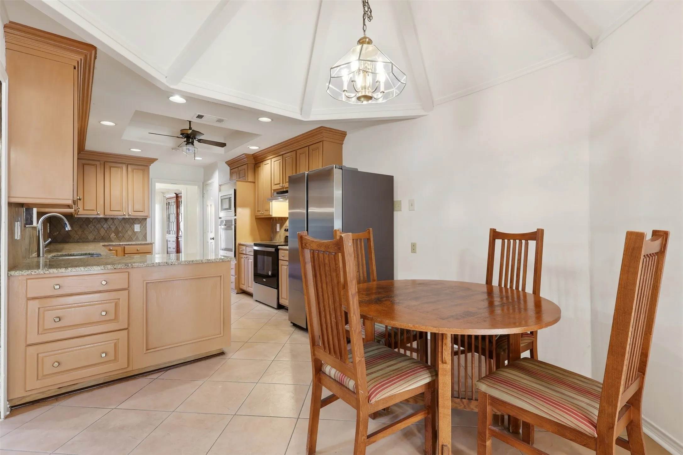 Kitchen featuring wood cabinetry, light-toned tiled flooring, granite countertops, and stainless steel appliances