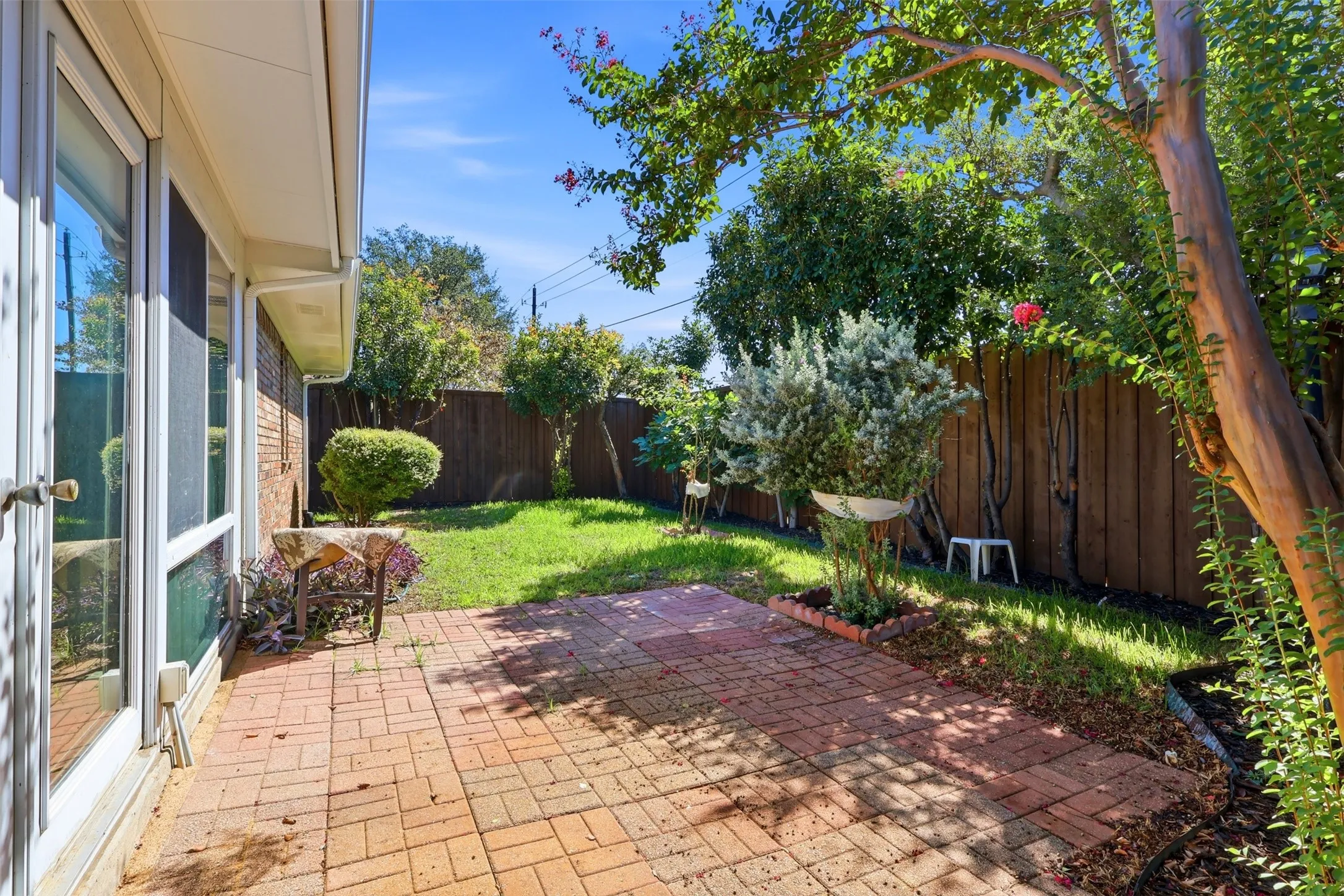 Brick patio with a manicured lawn, mature trees, and privacy fencing