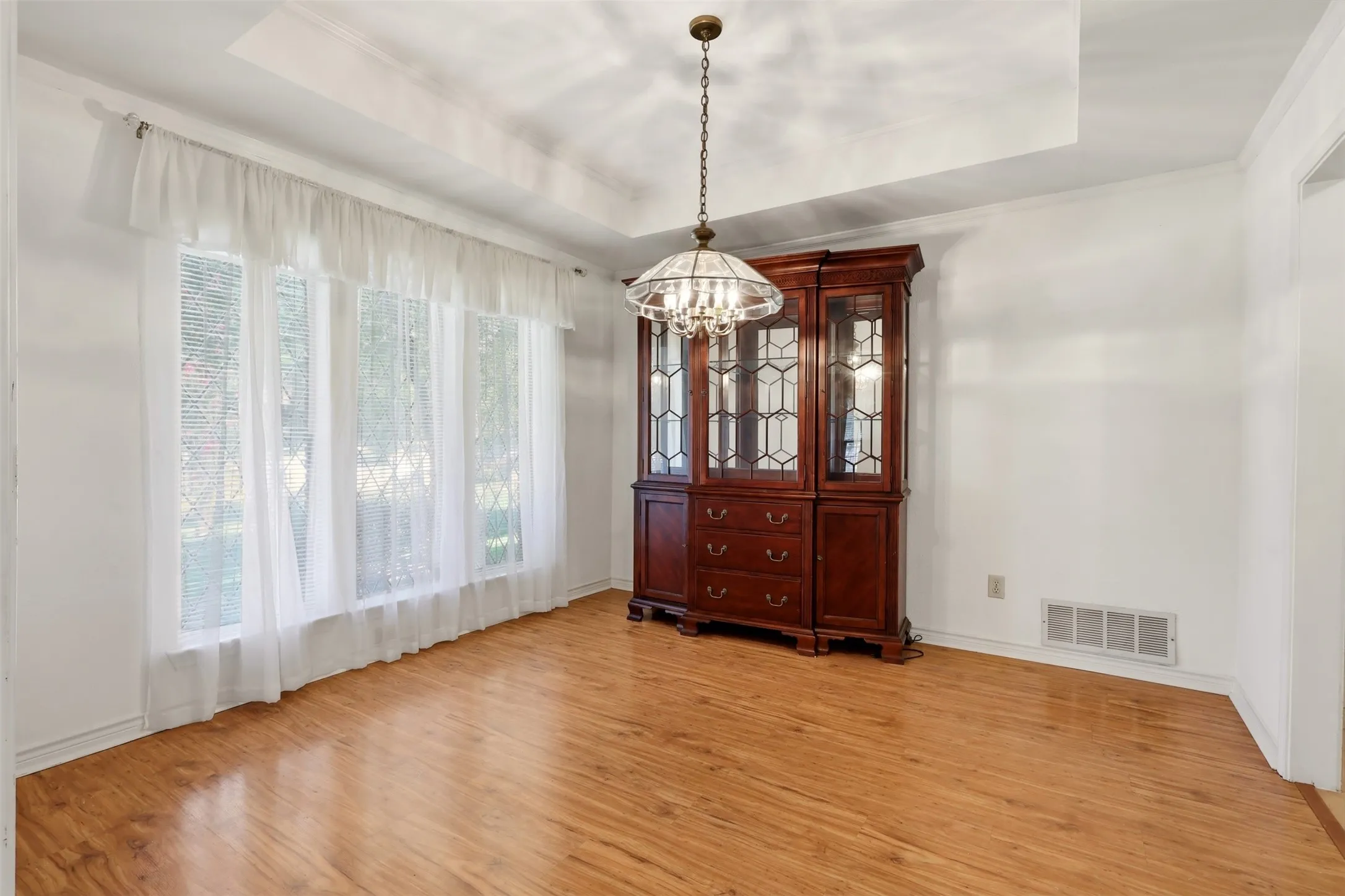 Tray ceiling, wood-finish flooring, chandelier, multiple windows, and white walls