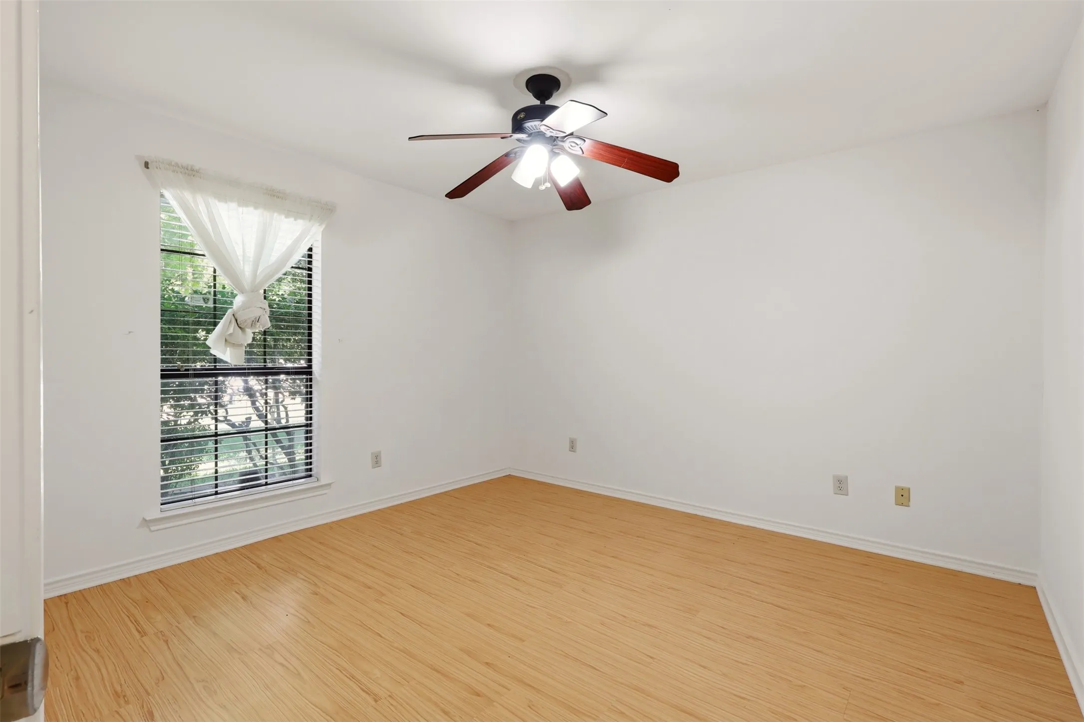 Light wood-finish flooring, a window with horizontal blinds, and a ceiling fan with light fixture