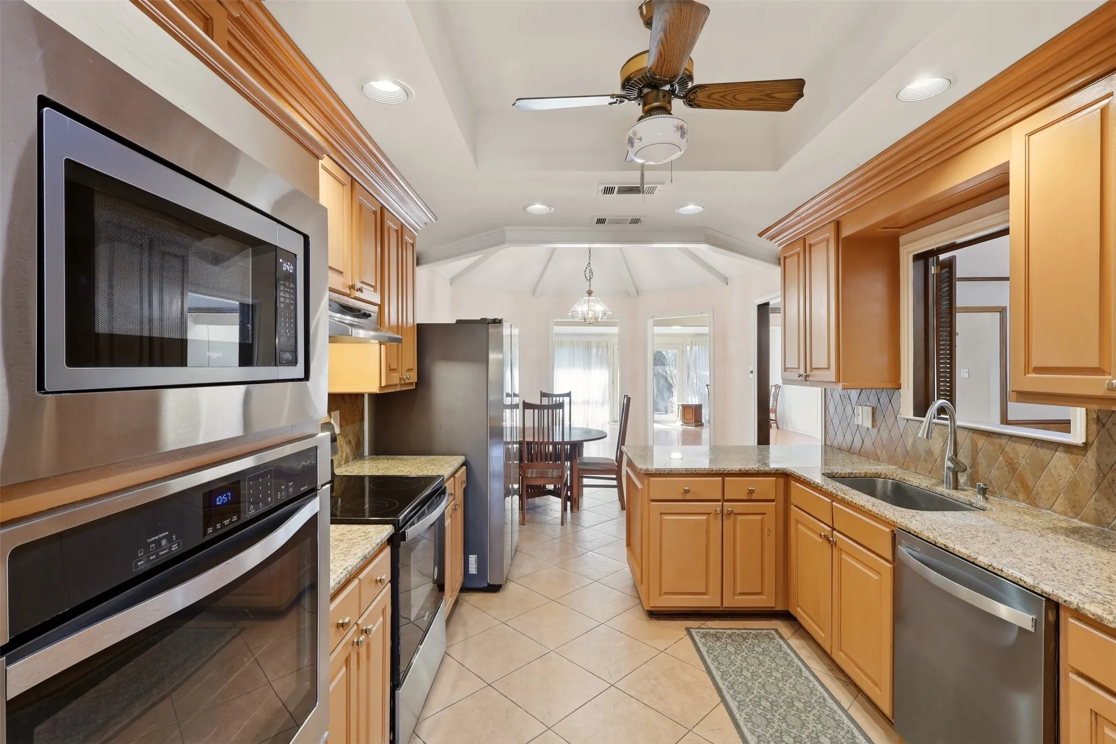 Galley kitchen featuring wood cabinetry, stainless steel appliances, granite countertops, and tile flooring