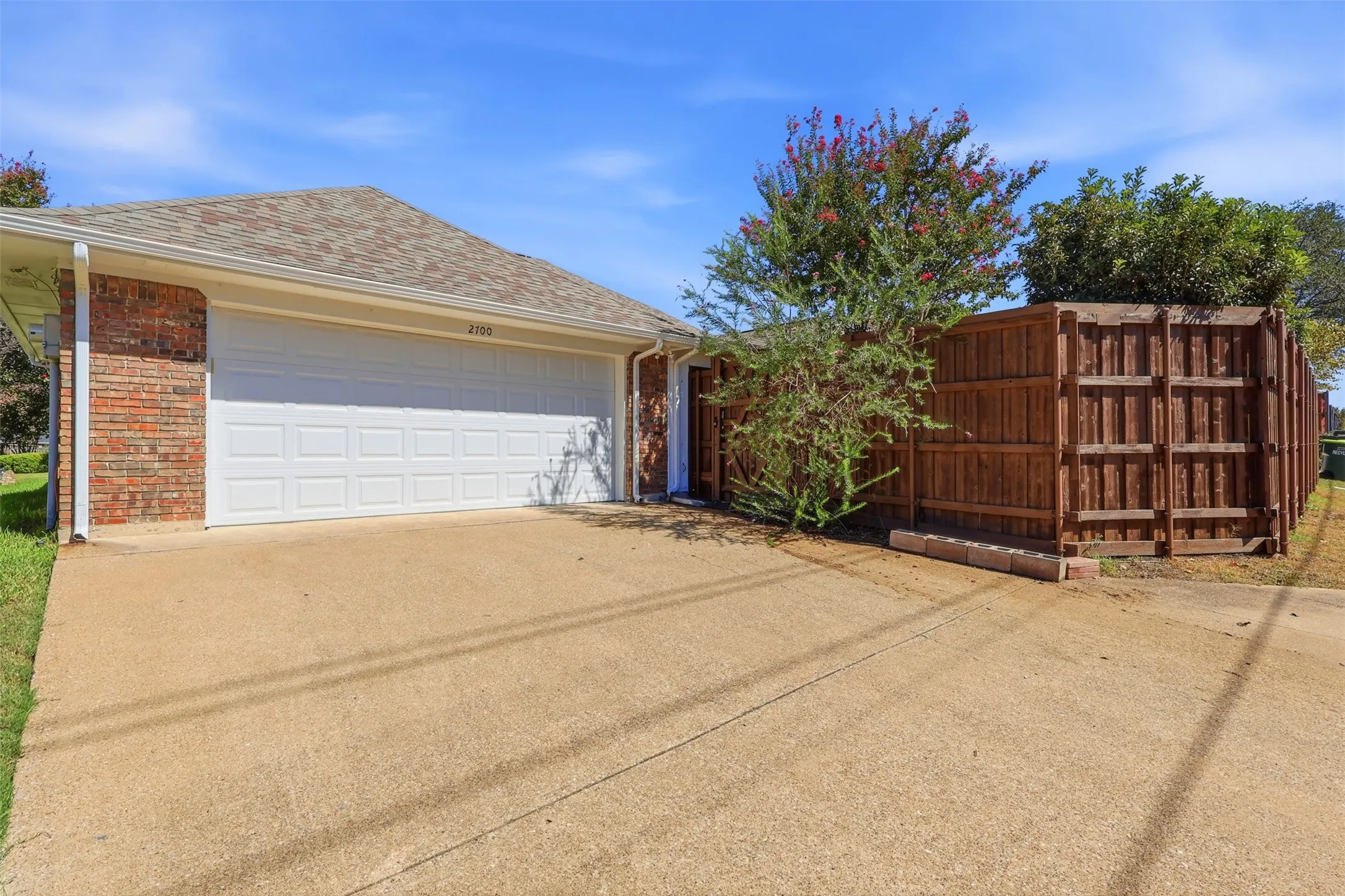 Brick exterior with an attached two-car garage, concrete driveway, and wood privacy fencing