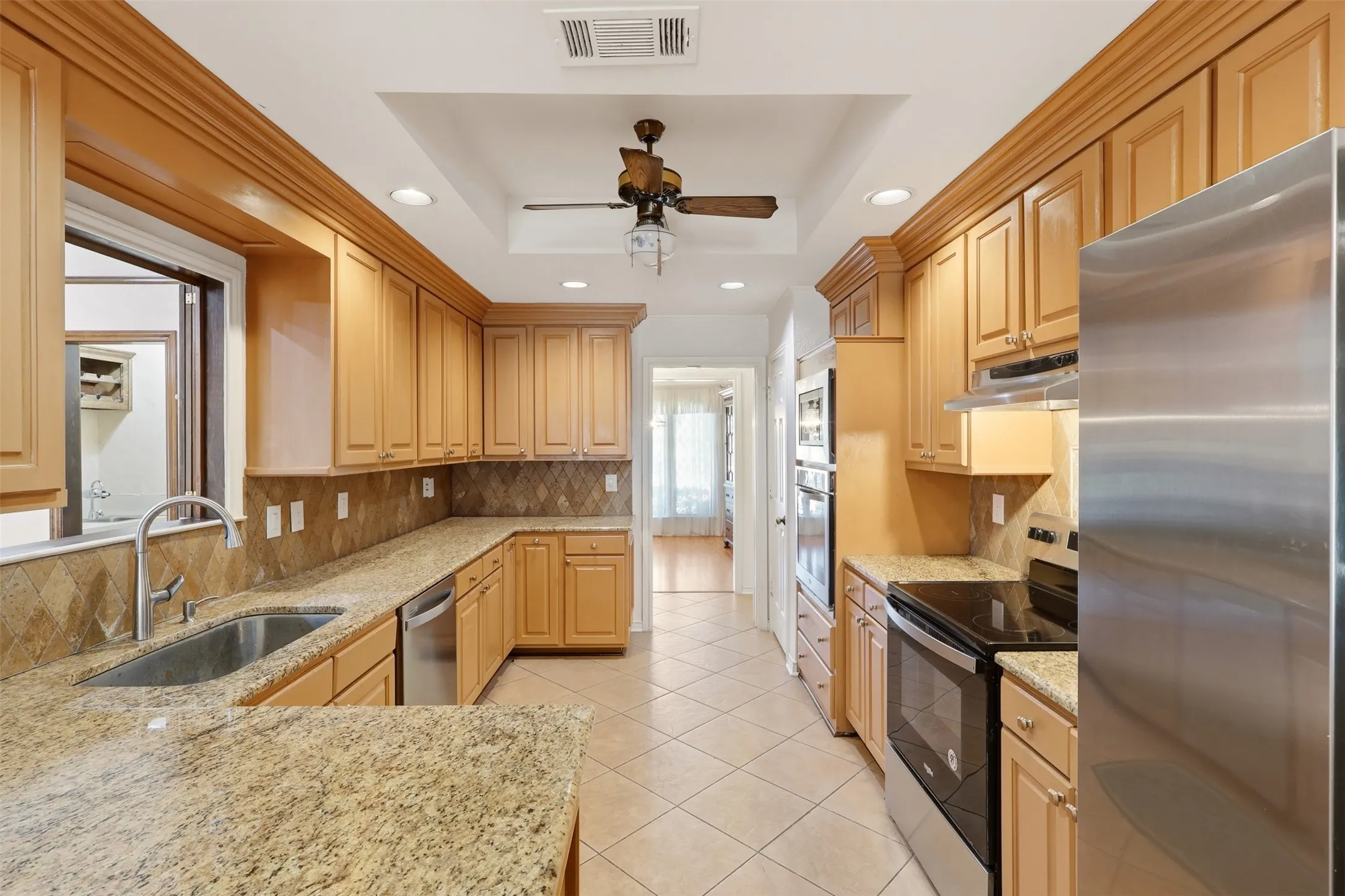 Gourmet kitchen featuring extensive cabinetry, granite countertops, stainless steel appliances, and a tray ceiling with a ceiling fan