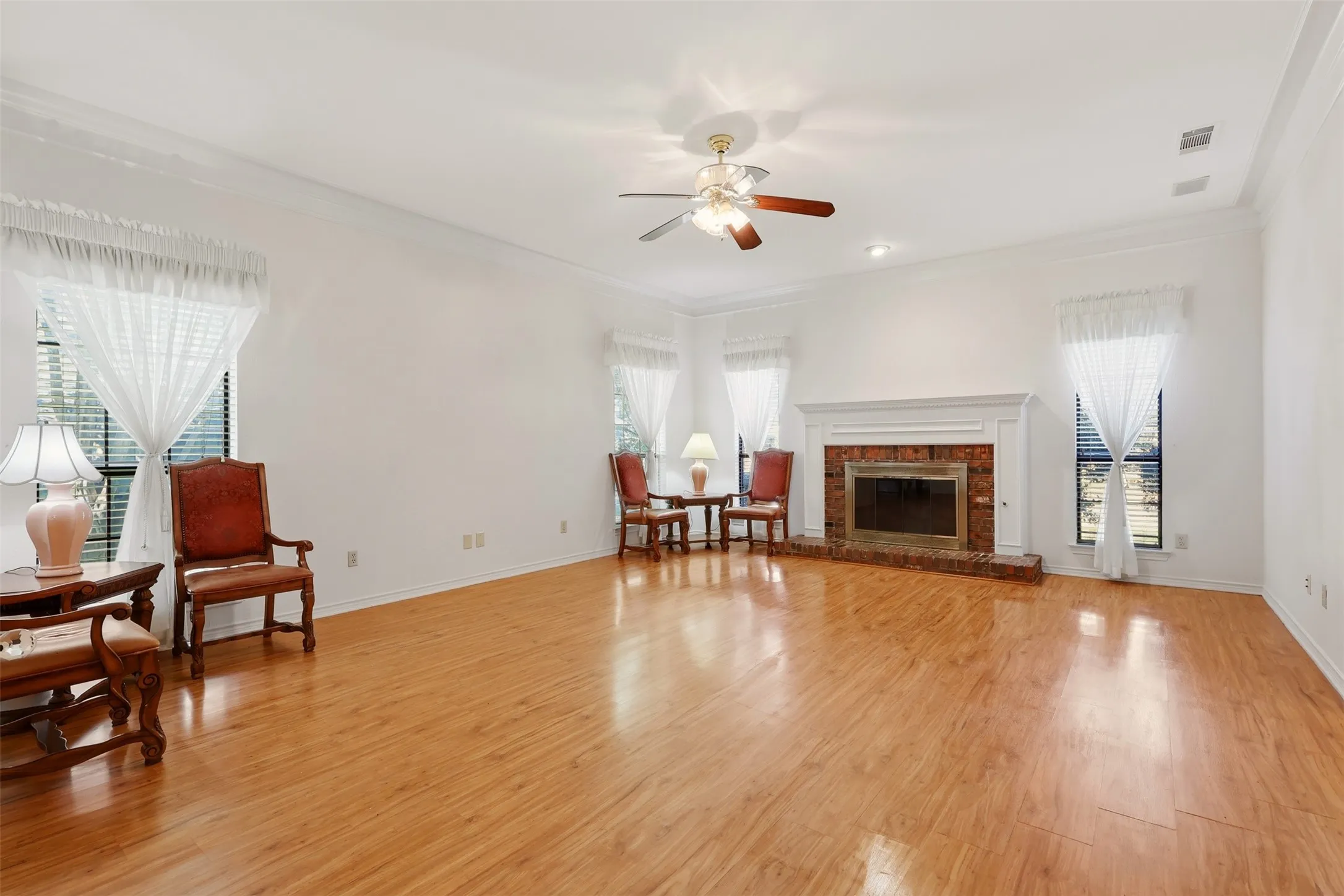 Spacious living room showcasing gleaming wood-finish flooring, recessed ceiling lighting, and a ceiling fan