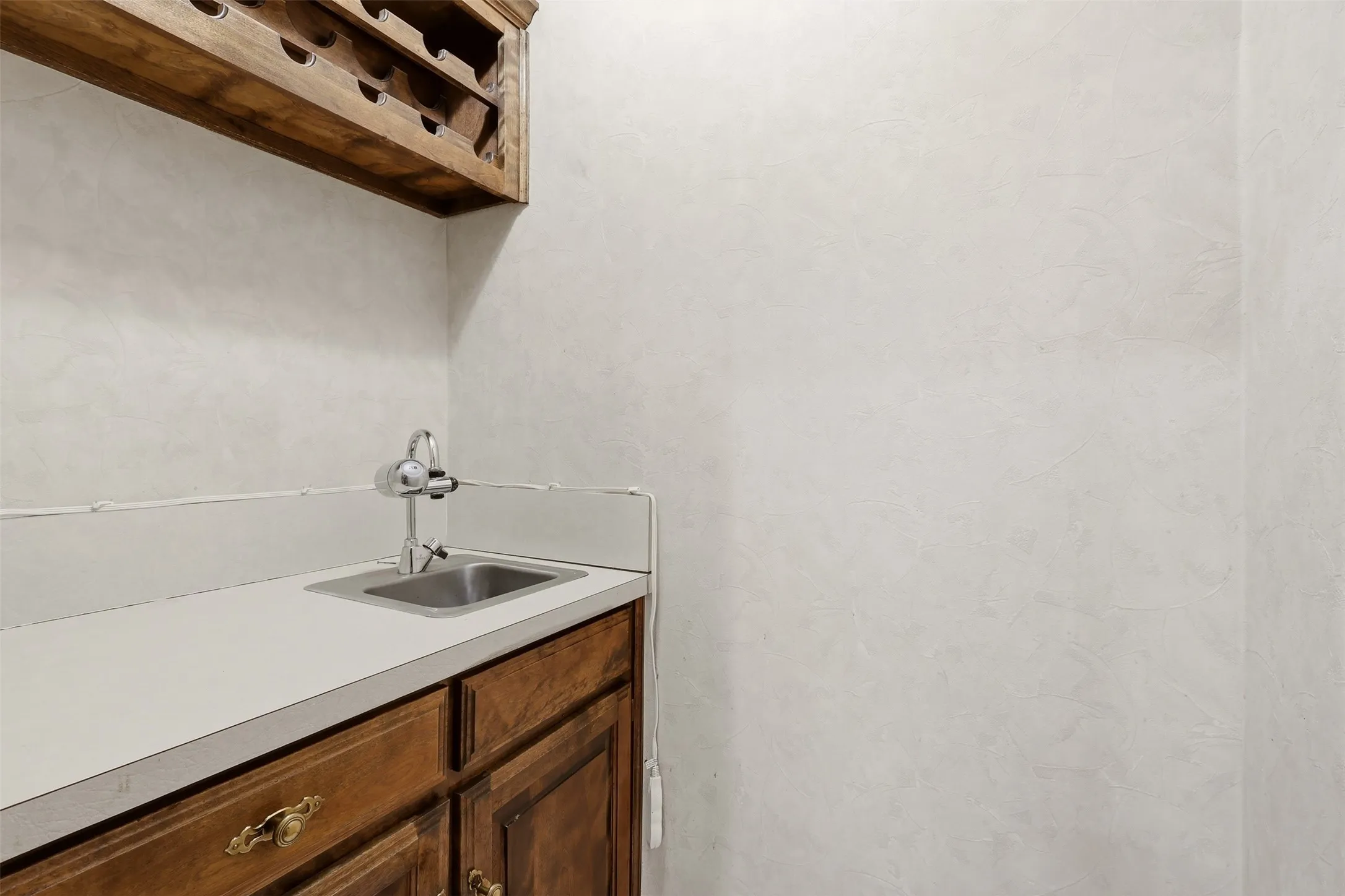 Built-in wood cabinetry with decorative hardware, integrated stainless steel sink, and wood-finish wine rack